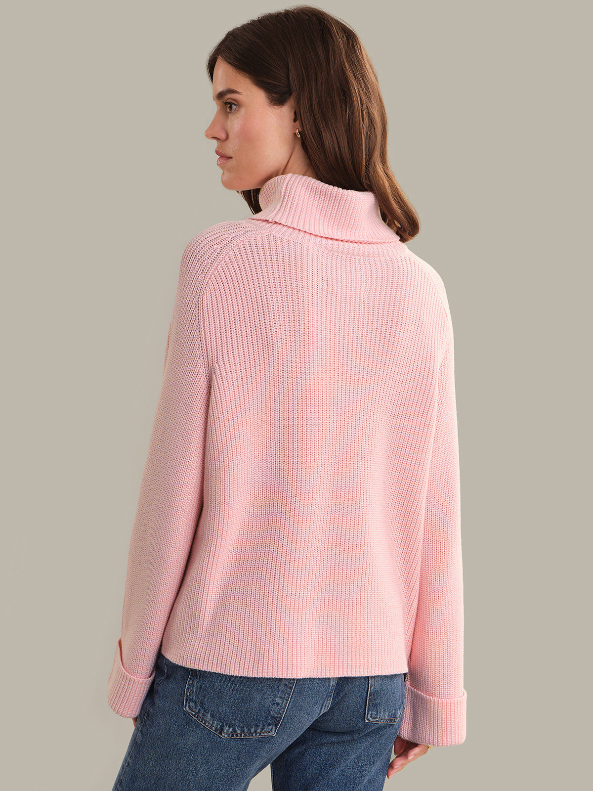 Woman wearing a pink sweater and blue jeans on a beige background