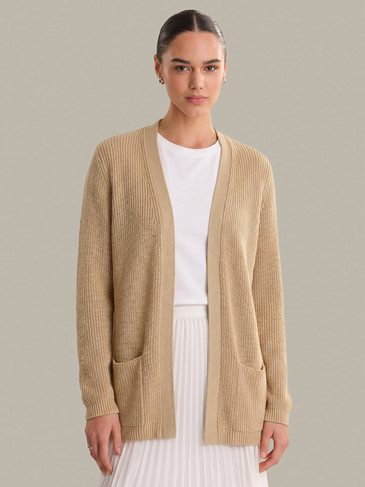 Woman wearing a beige cardigan over a white shirt and skirt on a neutral background