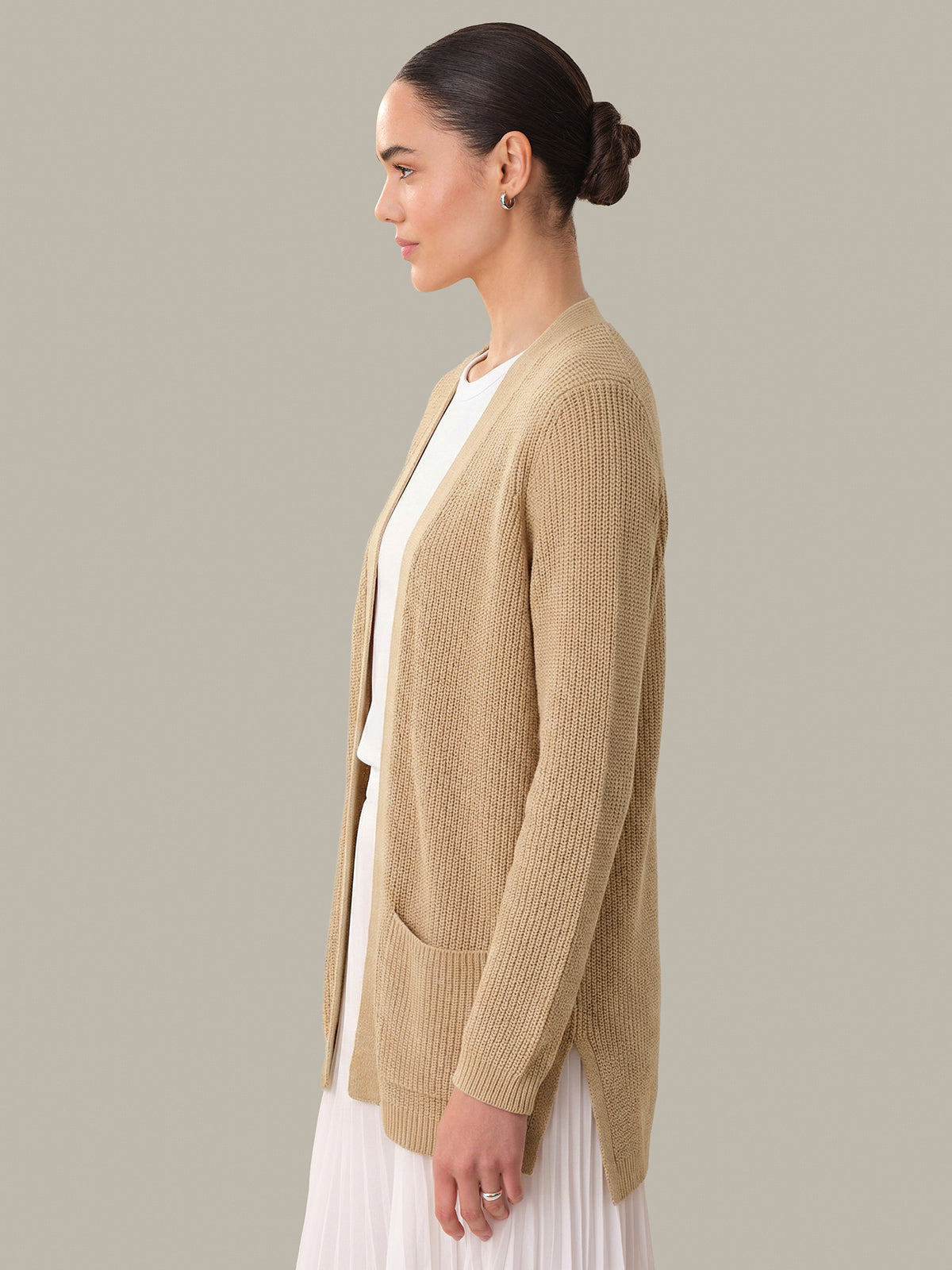 Woman wearing a beige cardigan over a white top on a neutral background