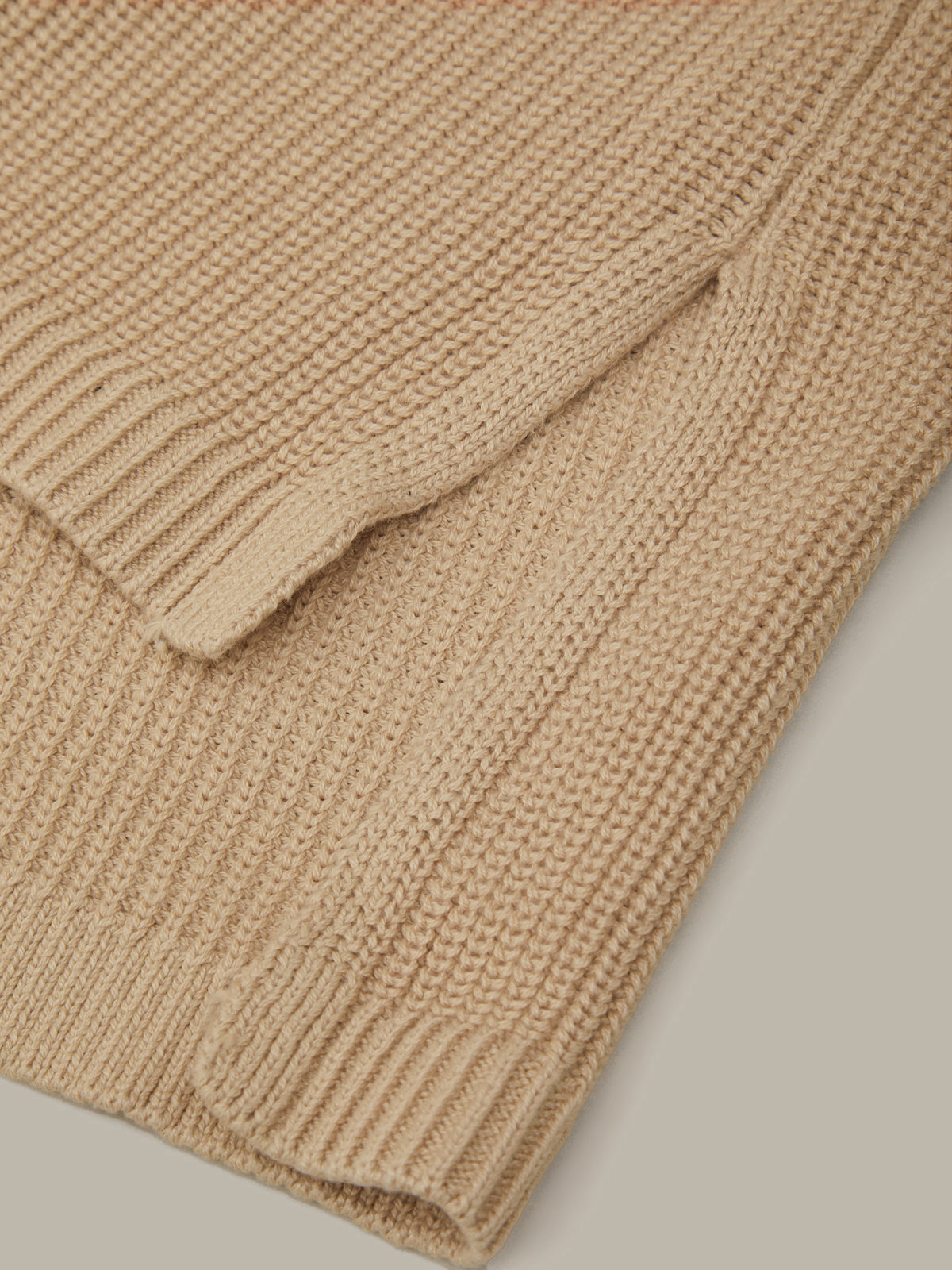 Close-up of a beige knitted sweater on a light gray background