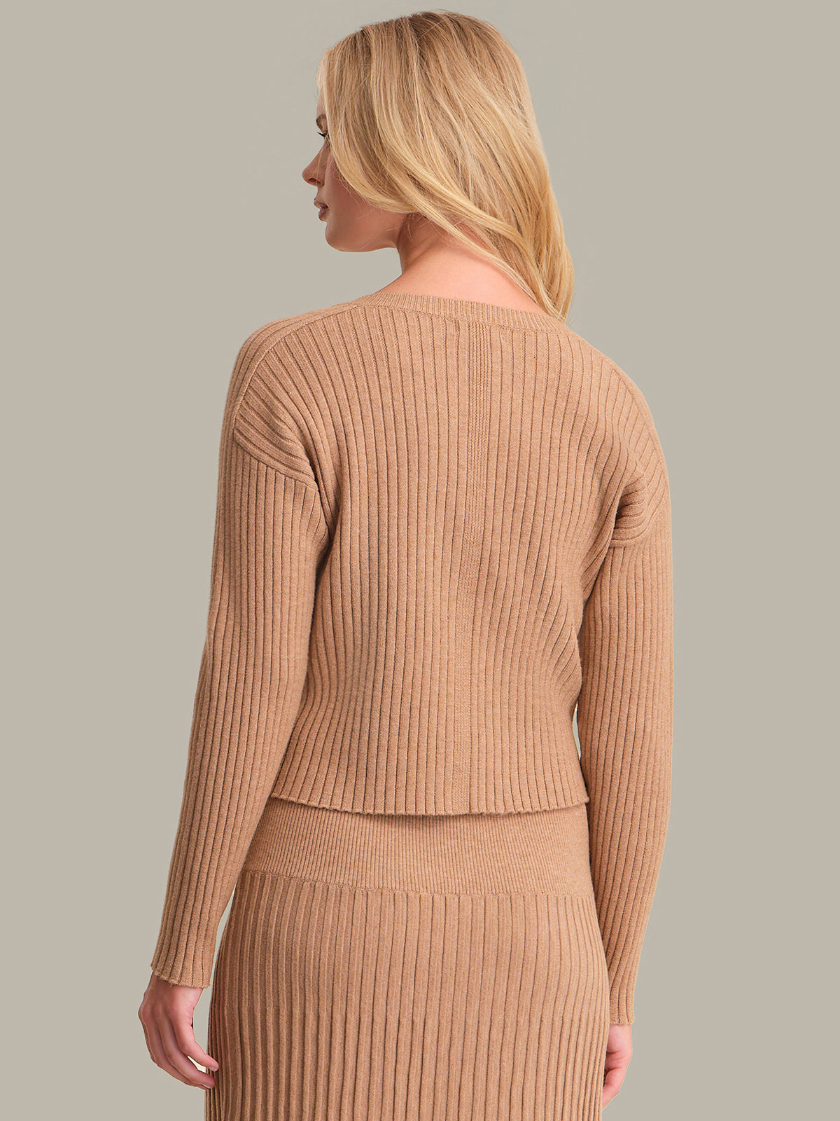 Woman wearing a brown ribbed sweater and skirt set against a neutral background