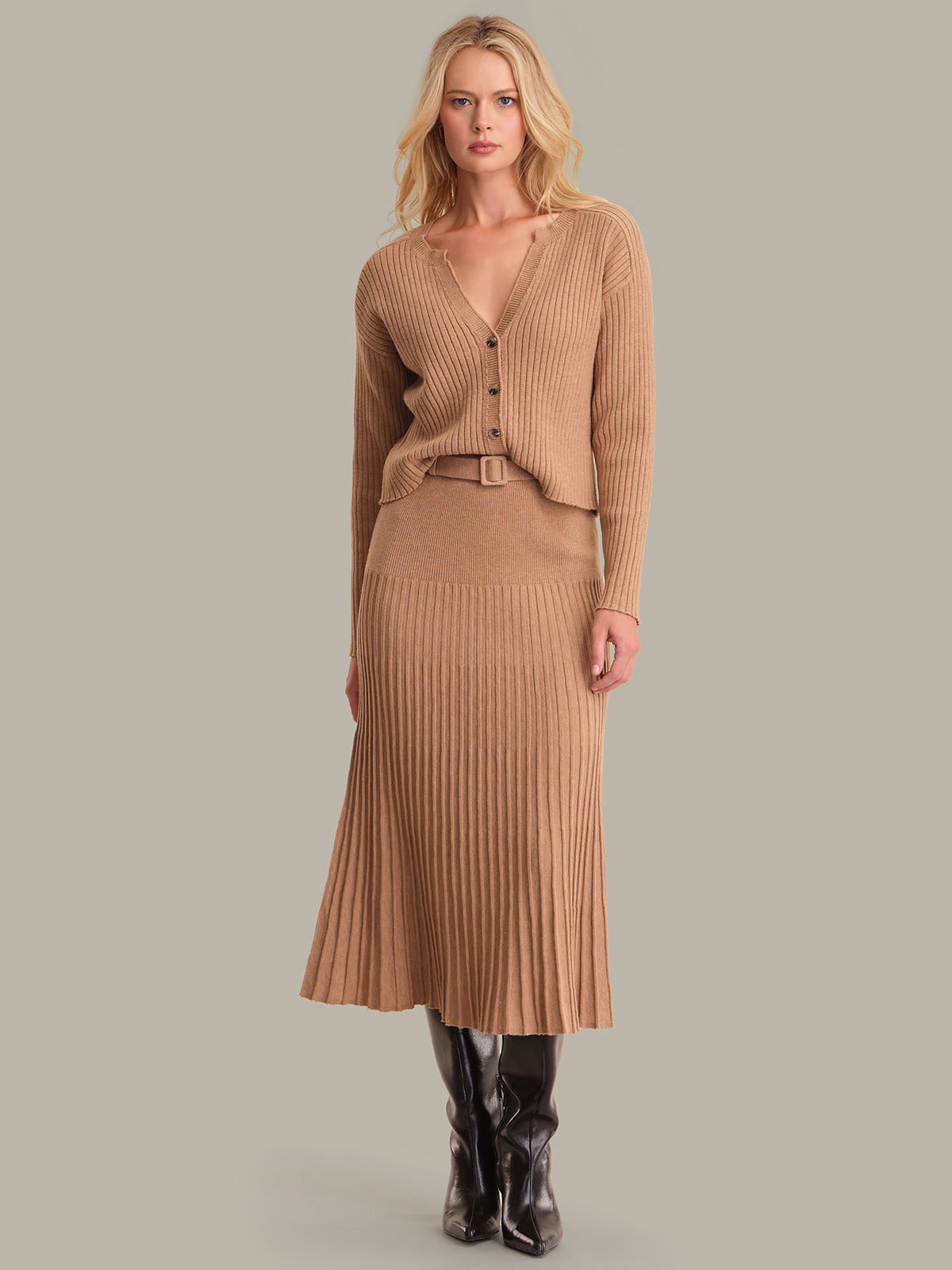Woman wearing a brown ribbed sweater and skirt set with black boots on a gray background