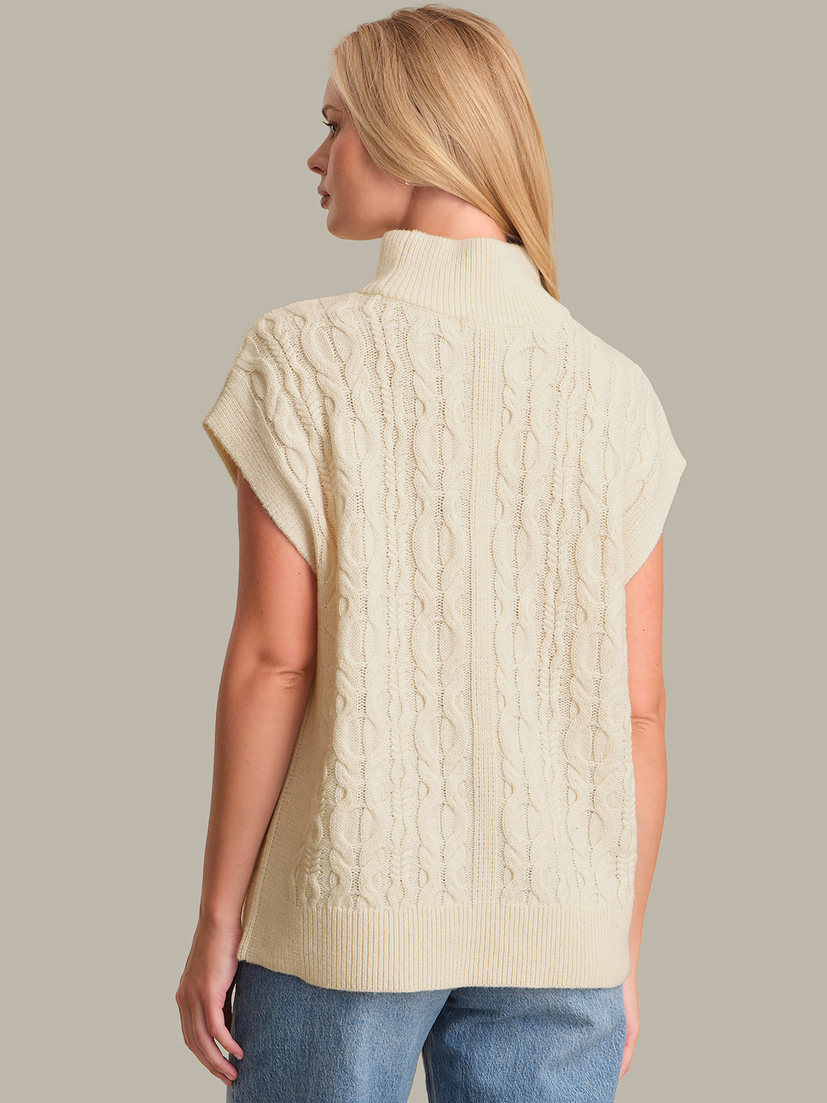 Woman wearing a cream-colored cable knit vest against a neutral background