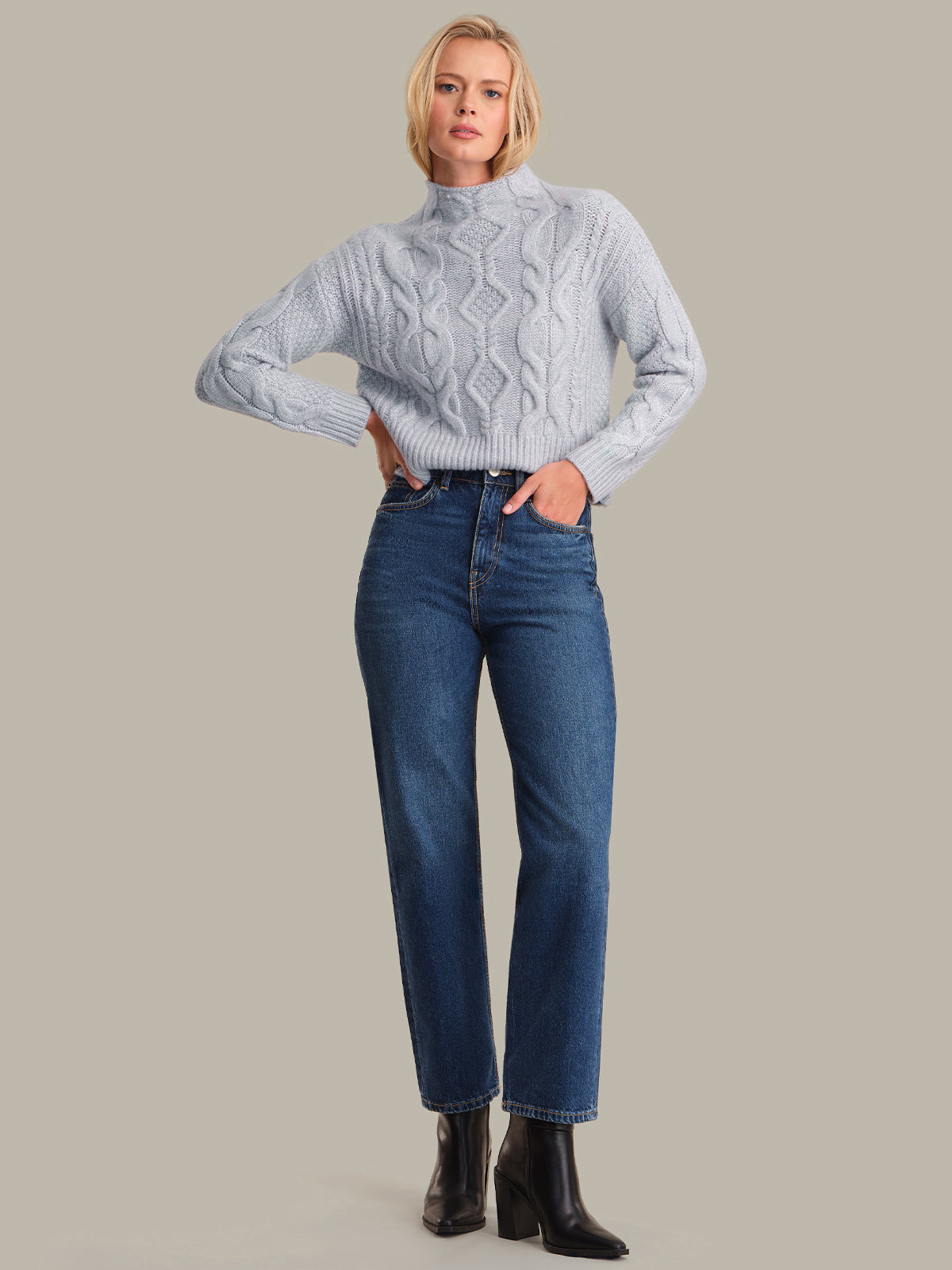 Woman wearing a light blue cable knit sweater and blue jeans on a gray background