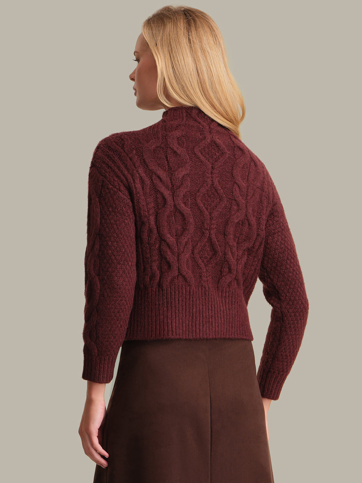 Woman wearing a burgundy cable knit sweater against a neutral background