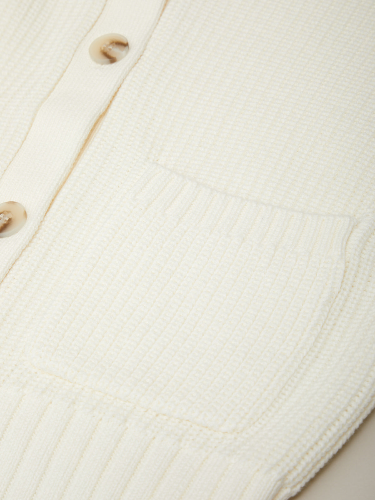 Close-up of a white ribbed knit cardigan with buttons.