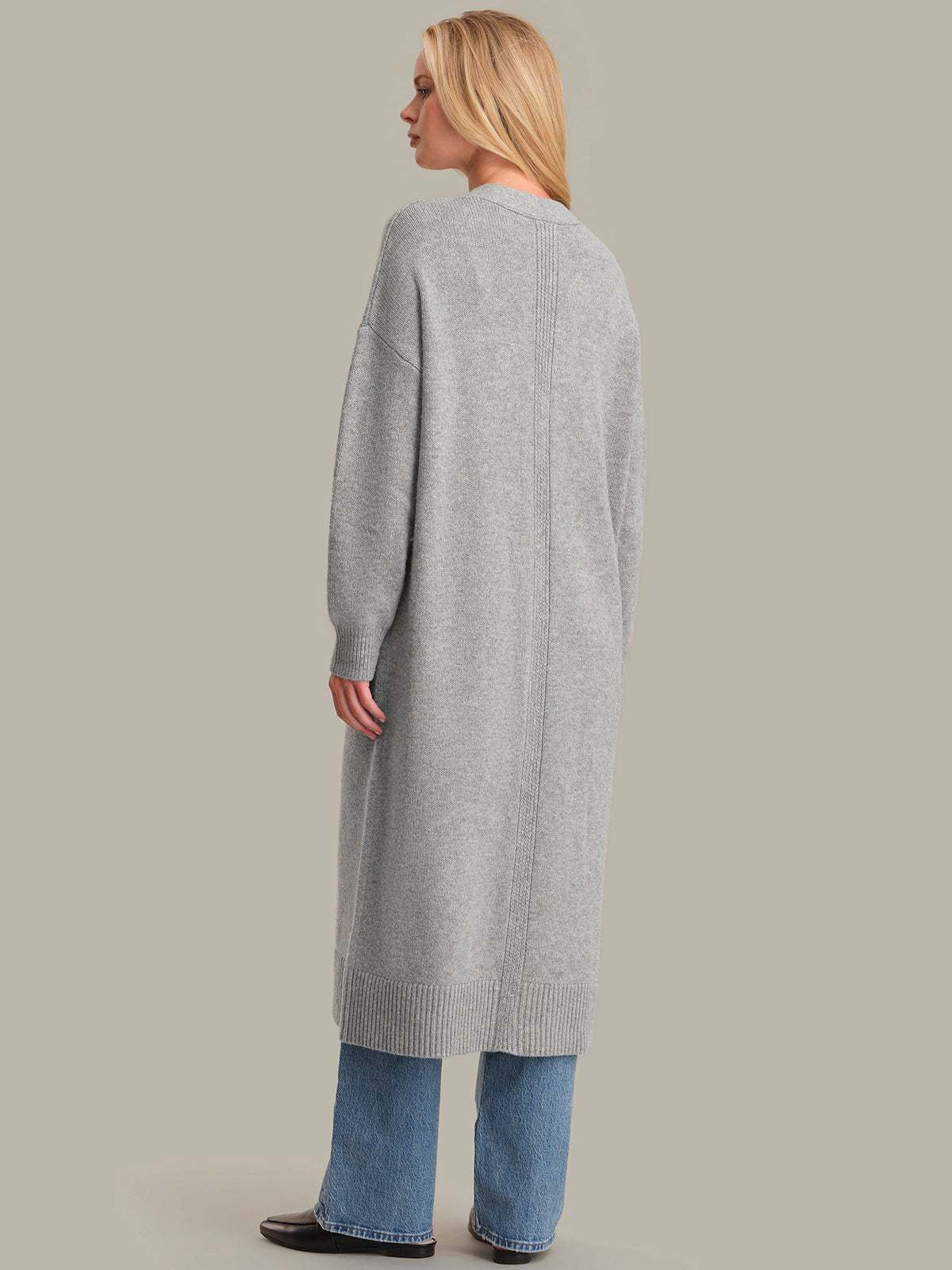 Person wearing a long gray cardigan and blue jeans on a beige background