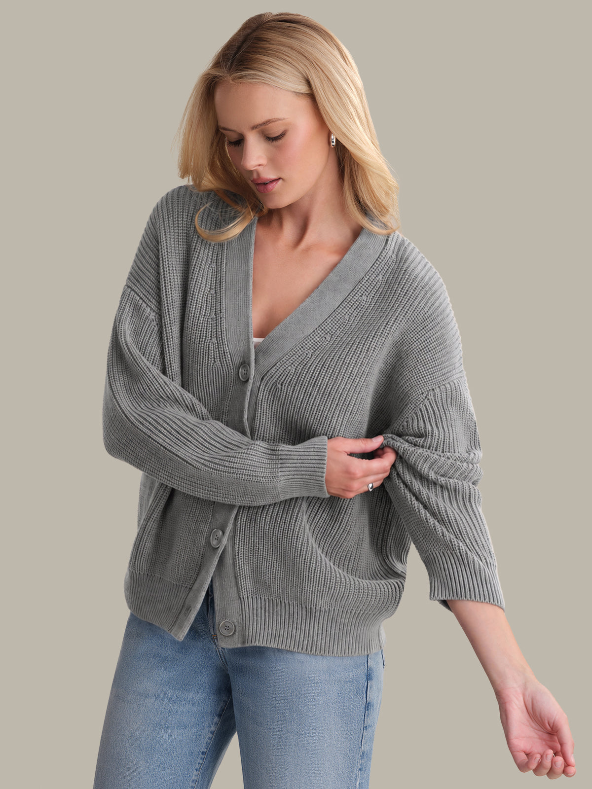 Woman wearing a gray cardigan over a white top with blue jeans on a beige background