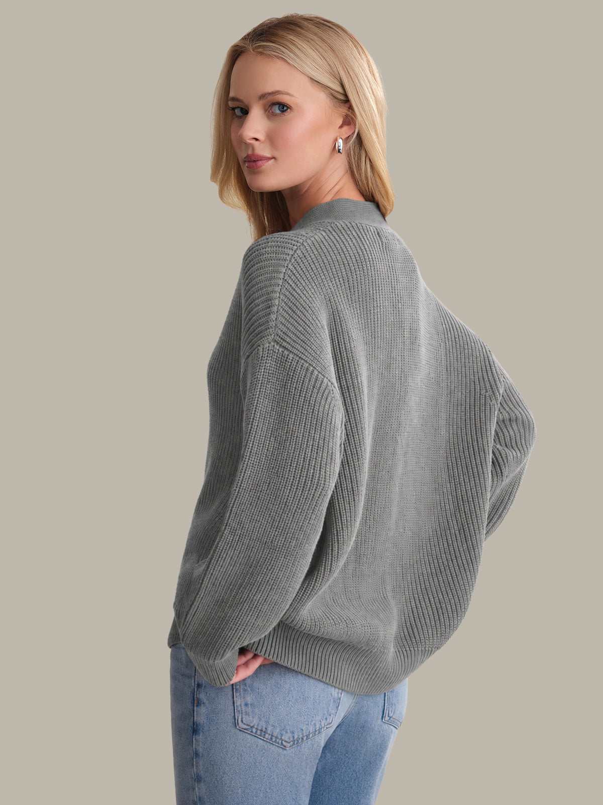 Woman wearing a gray sweater and blue jeans against a plain background