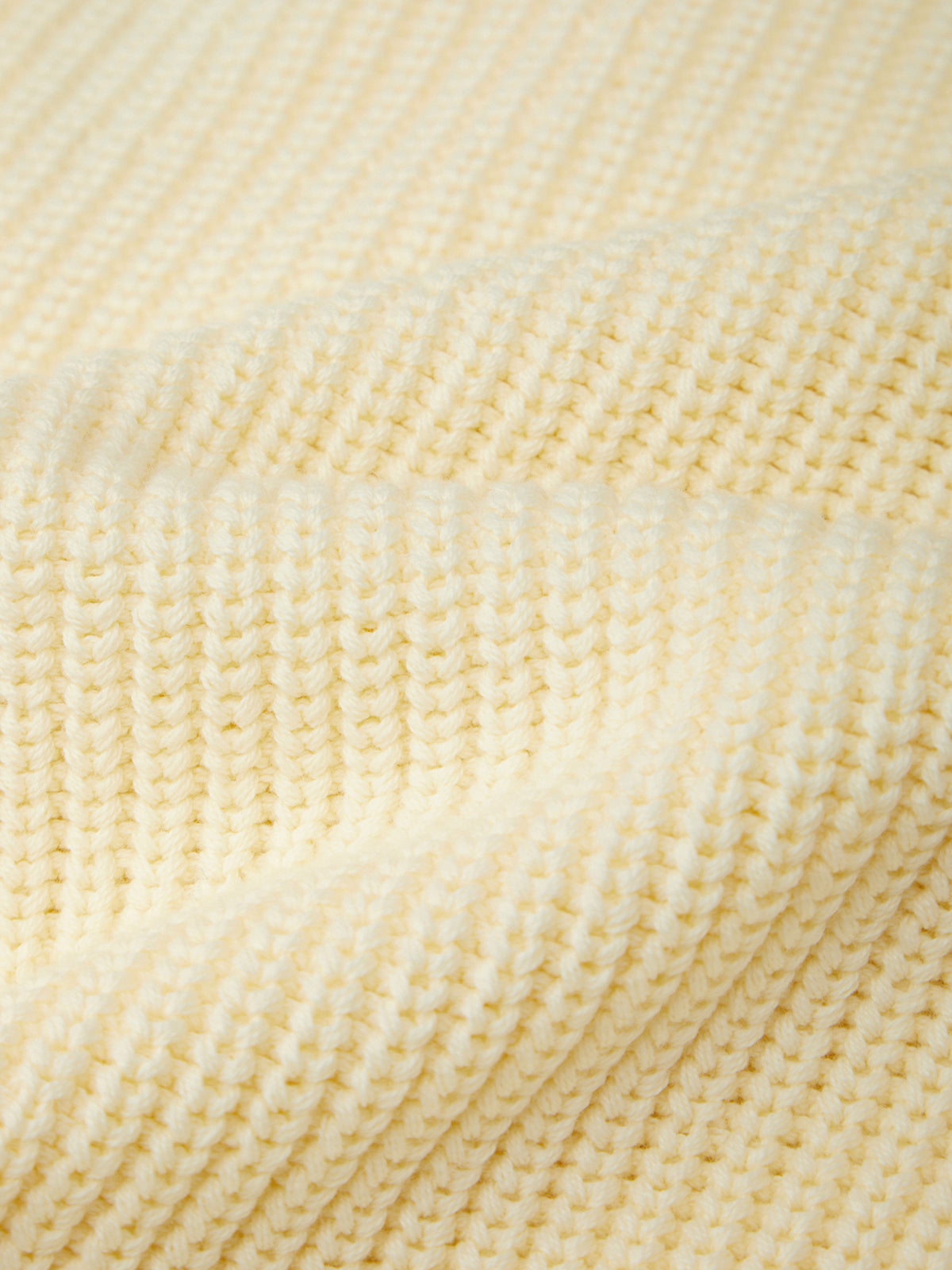 Close-up of a cream-colored ribbed knit fabric texture, showing the detailed knit pattern and soft folds.