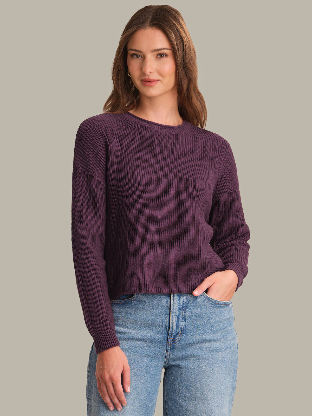 Woman wearing a purple sweater and blue jeans against a gray background