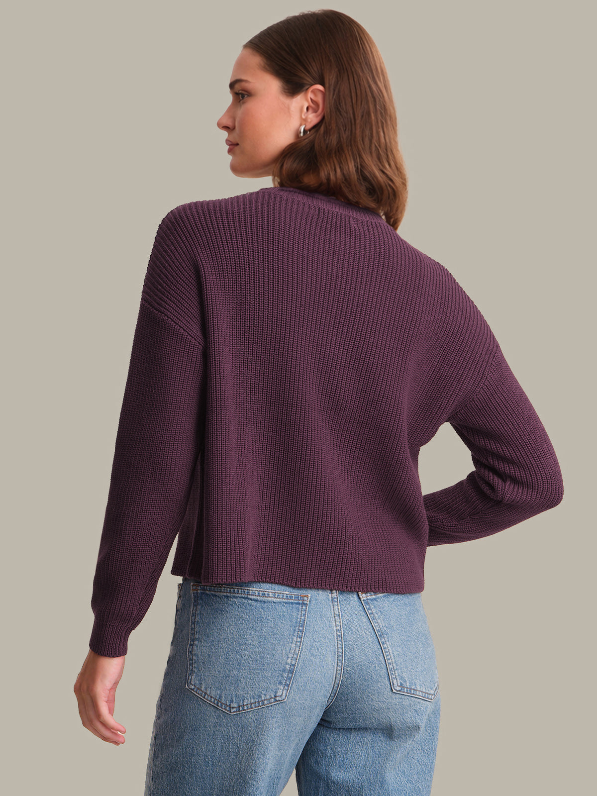 Woman wearing a purple sweater and blue jeans on a plain background