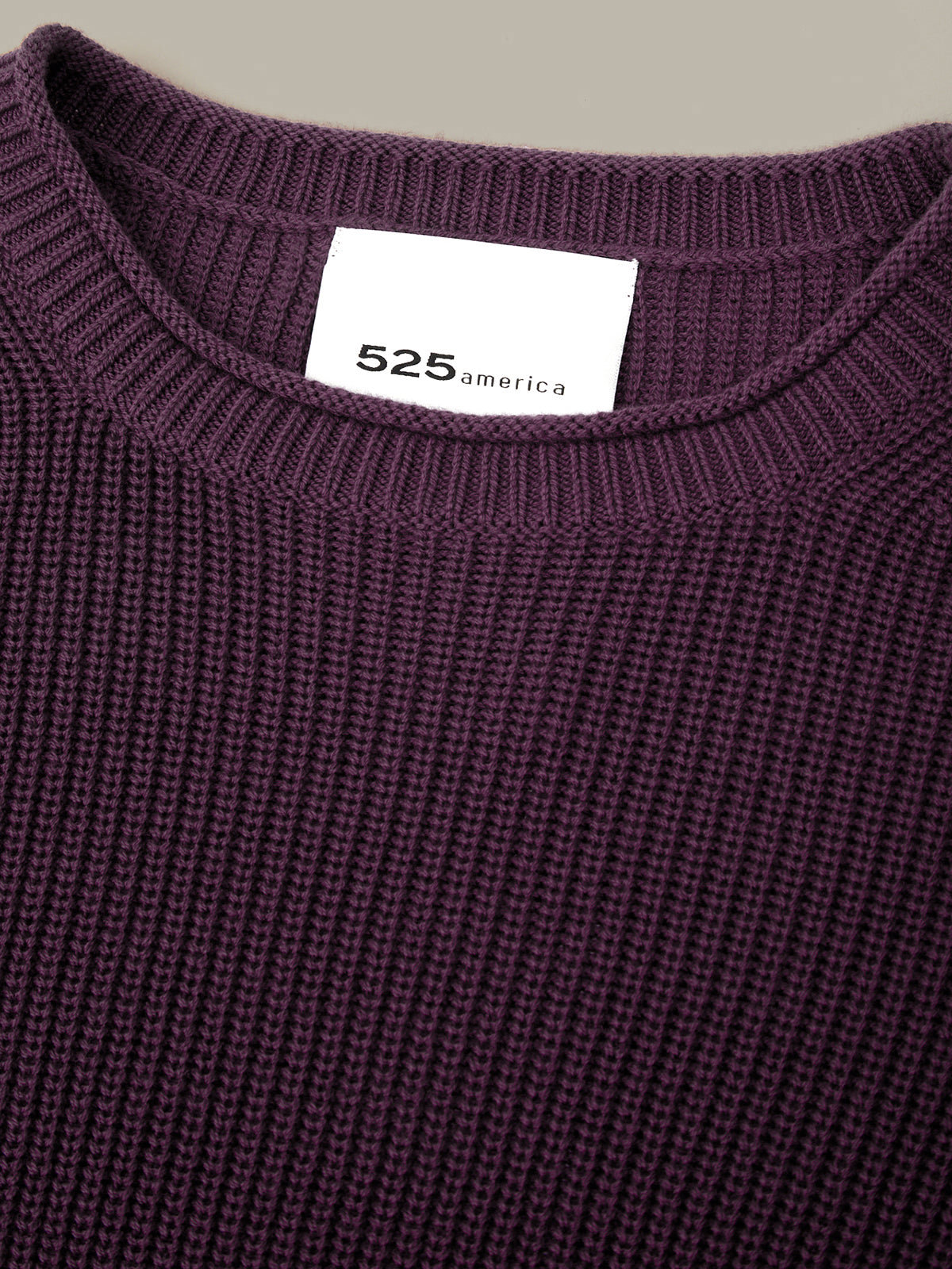 Close-up of a purple sweater with a visible brand label on a neutral background