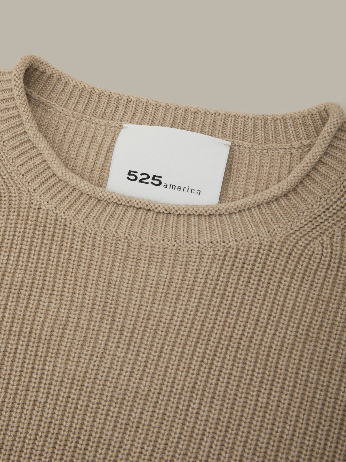 Close-up of a beige sweater with a white label displaying '525 america'.