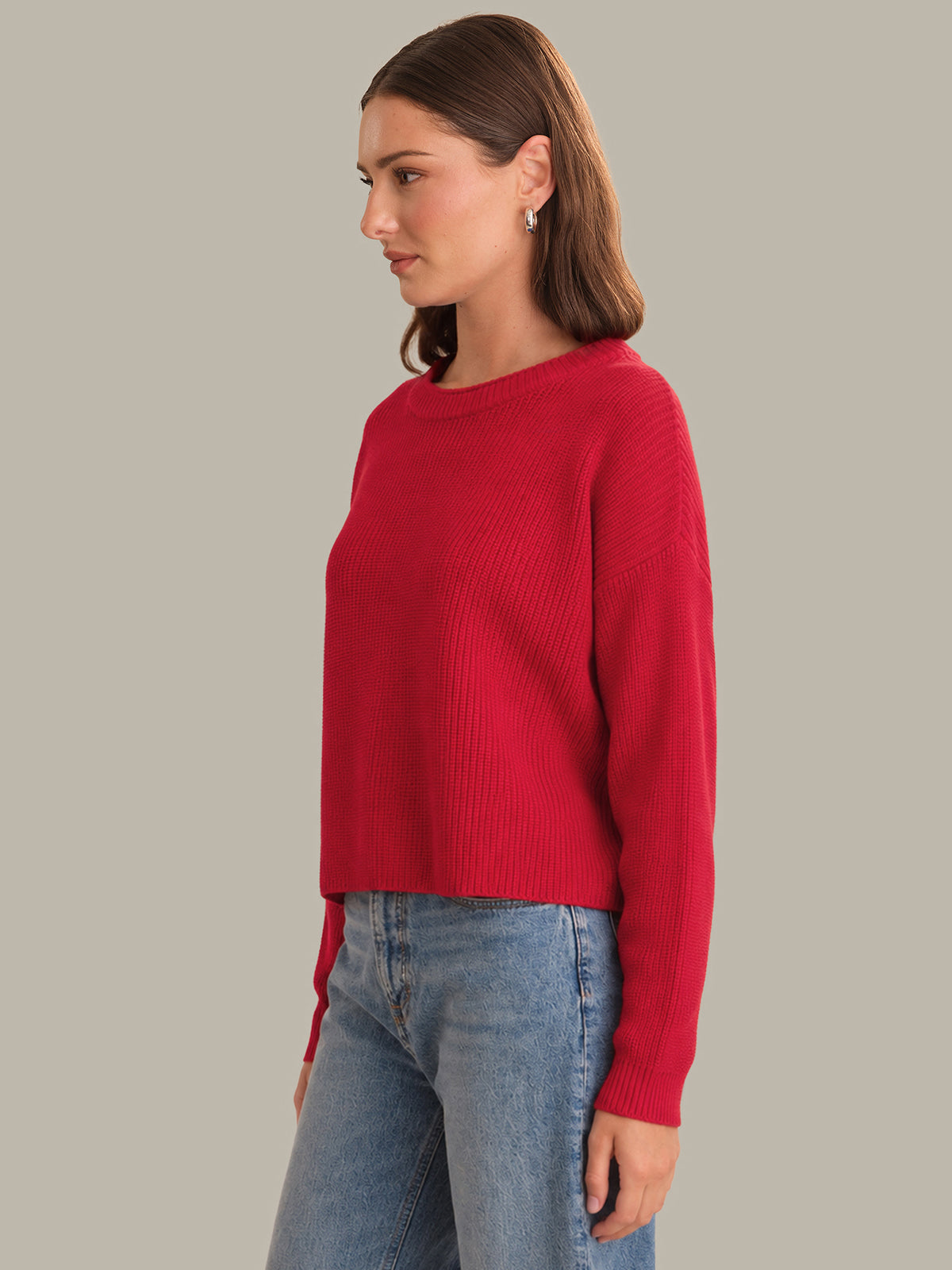 Woman wearing a red sweater and blue jeans on a plain background