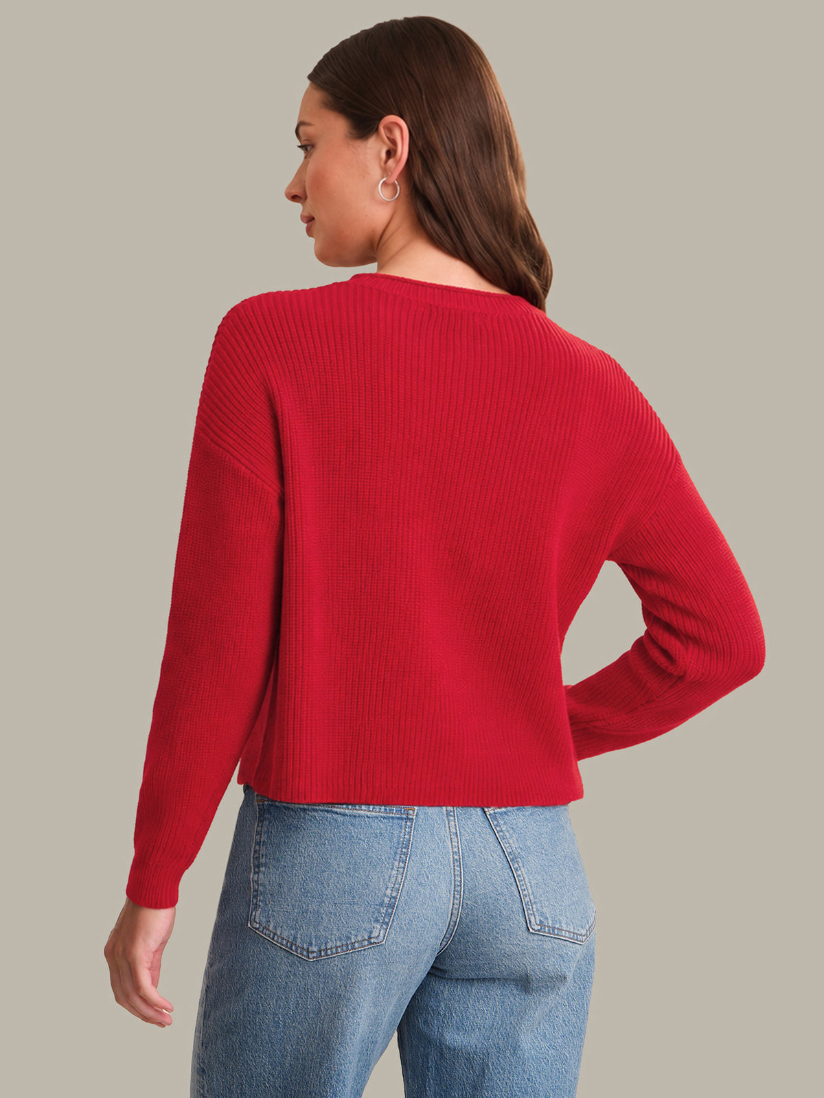 Woman wearing a red sweater and blue jeans on a plain background