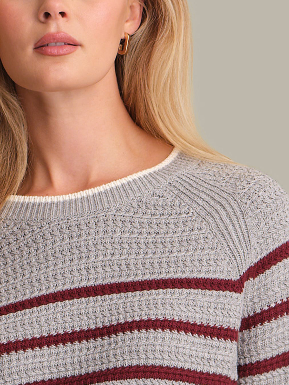 Close-up of a person wearing a gray and red striped sweater with a neutral background