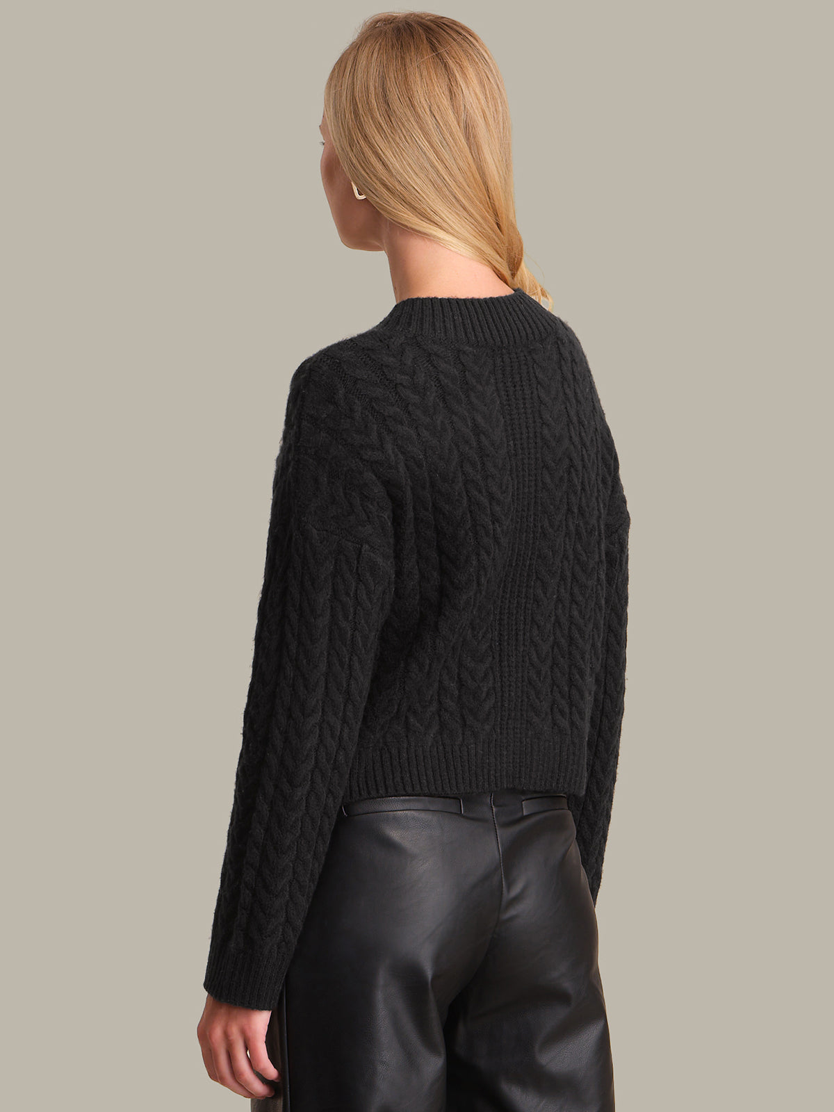 Person wearing a black cable knit sweater and black leather pants on a neutral background