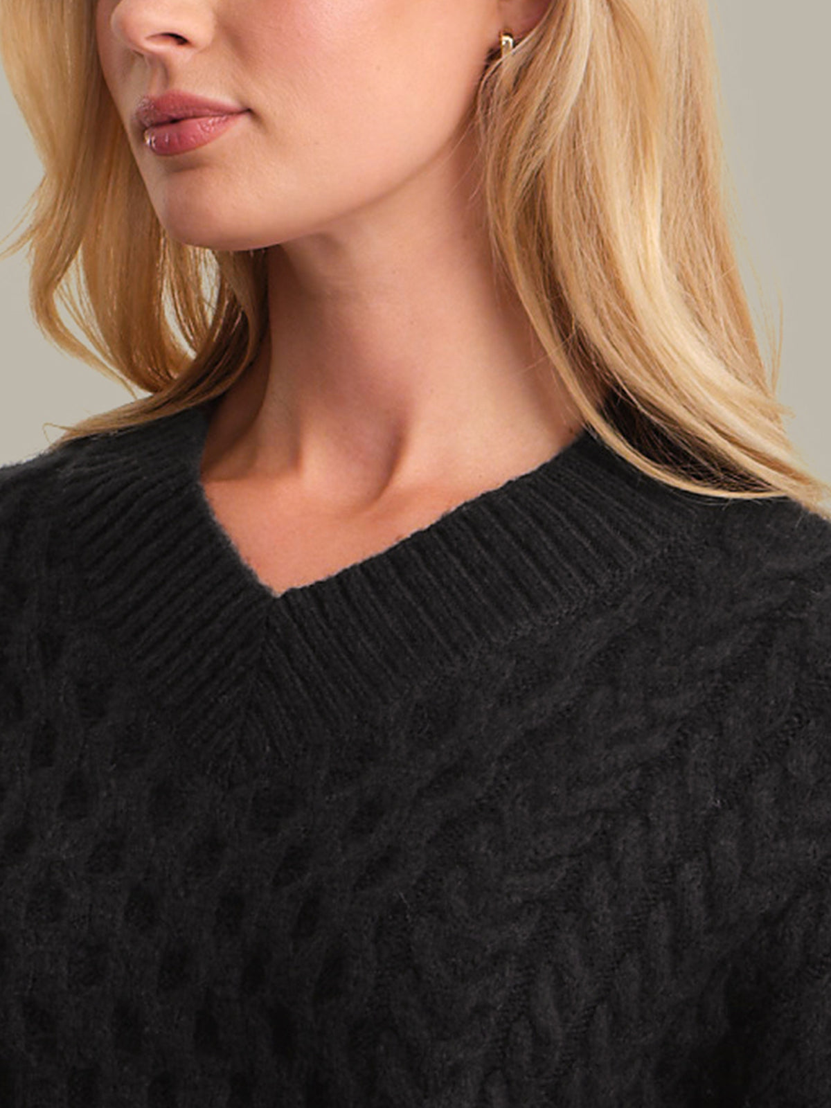 Close-up of a person wearing a black cable knit sweater with a neutral background