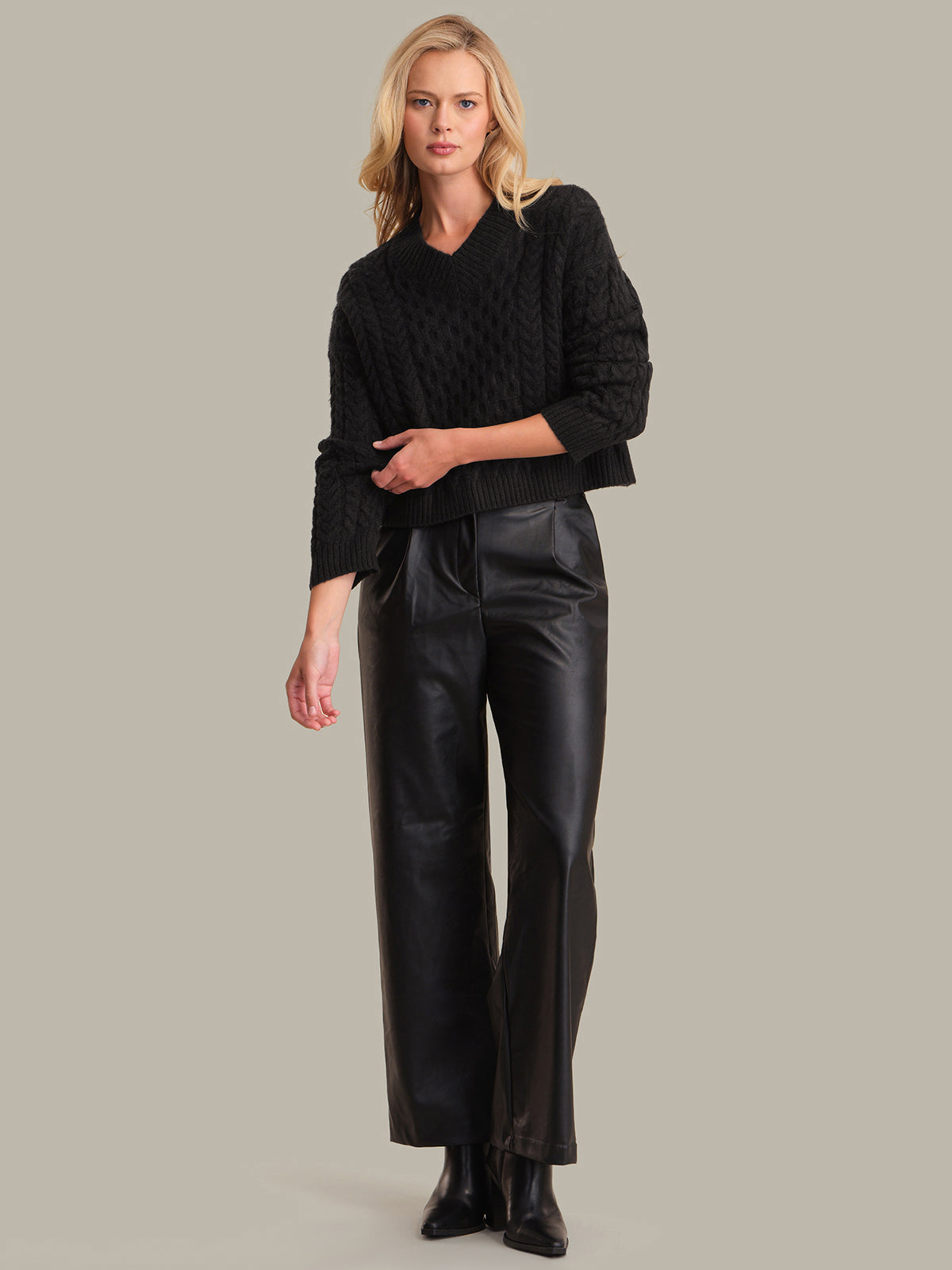 Woman wearing a black cable knit sweater and black leather pants on a gray background
