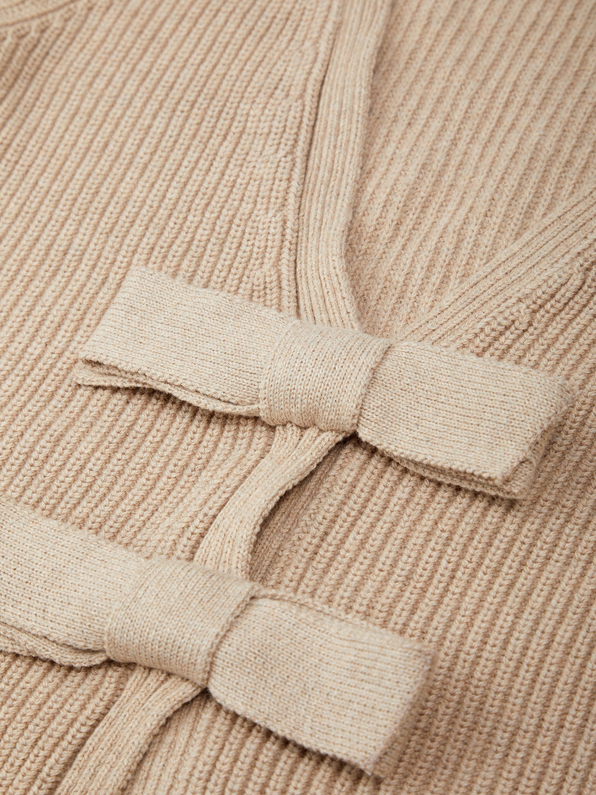 Close-up of a beige ribbed sweater with a bow detail.