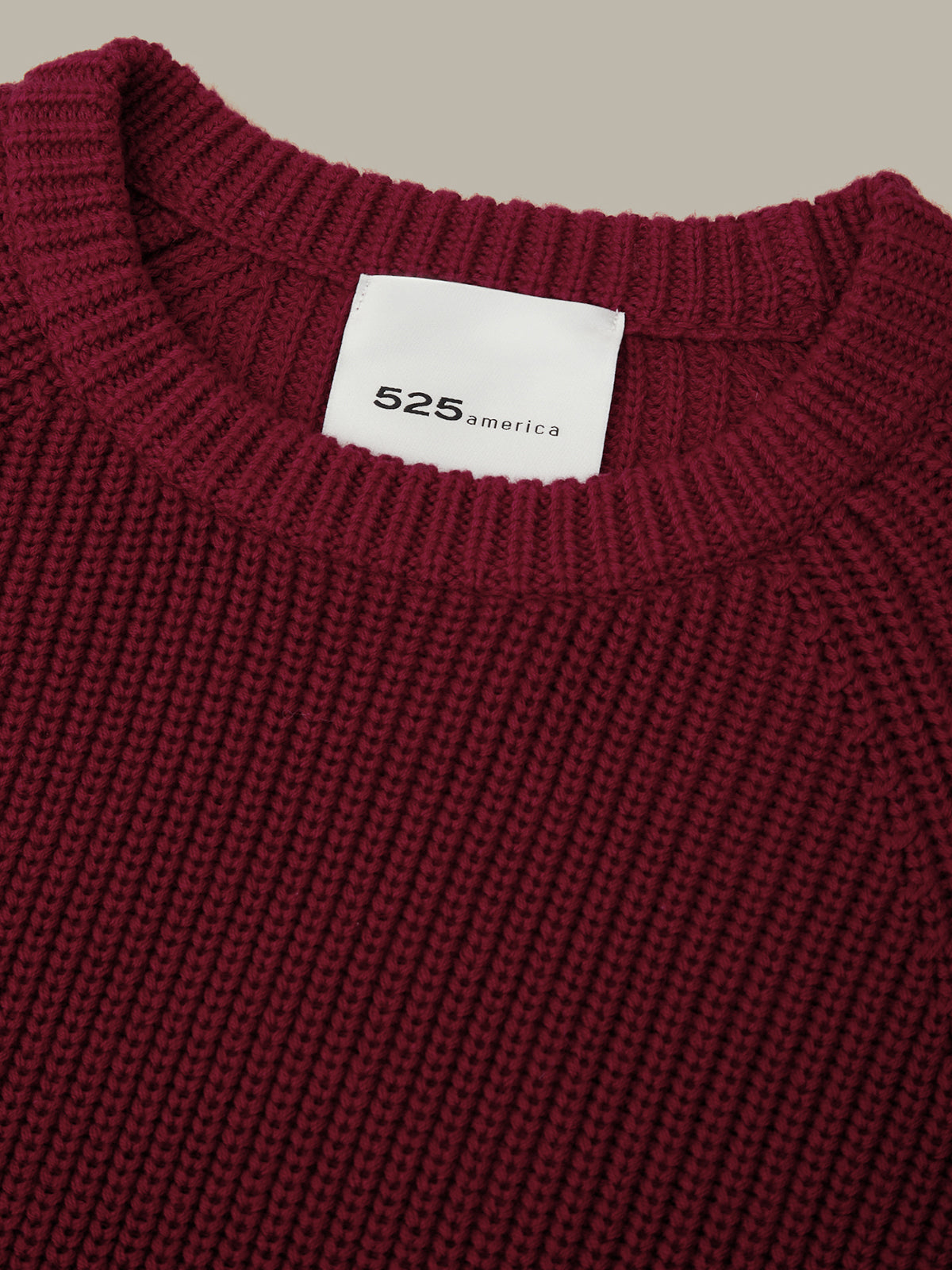 Close-up of a maroon sweater with a visible brand label on a beige background
