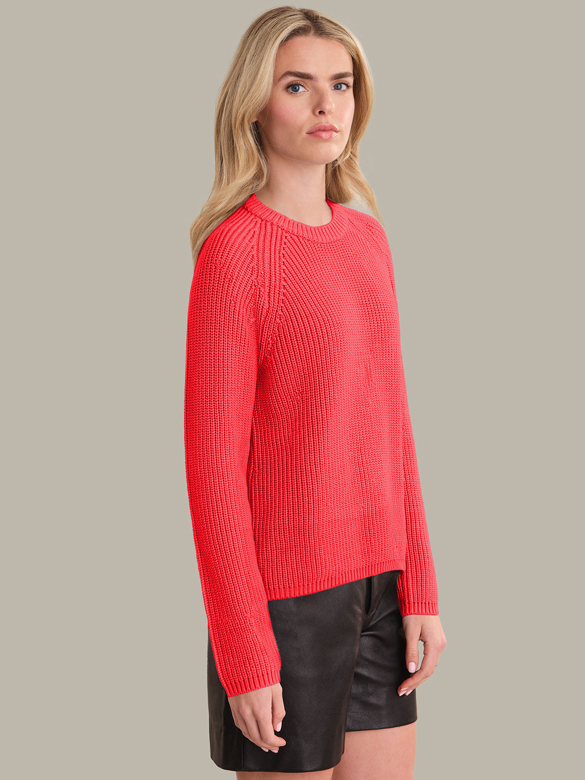 Woman wearing a red sweater and black shorts against a neutral background