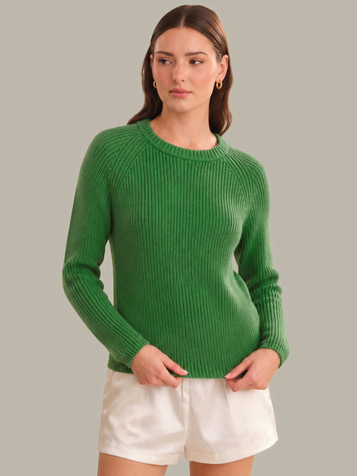 Woman wearing a green sweater and white shorts against a gray background