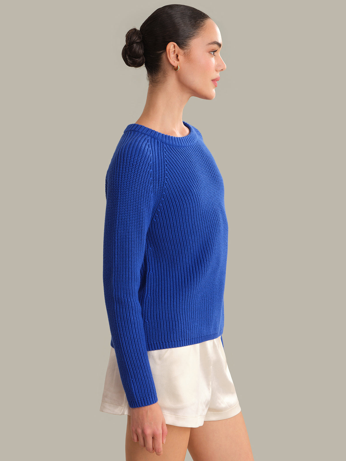 Woman wearing a blue sweater and white skirt against a gray background