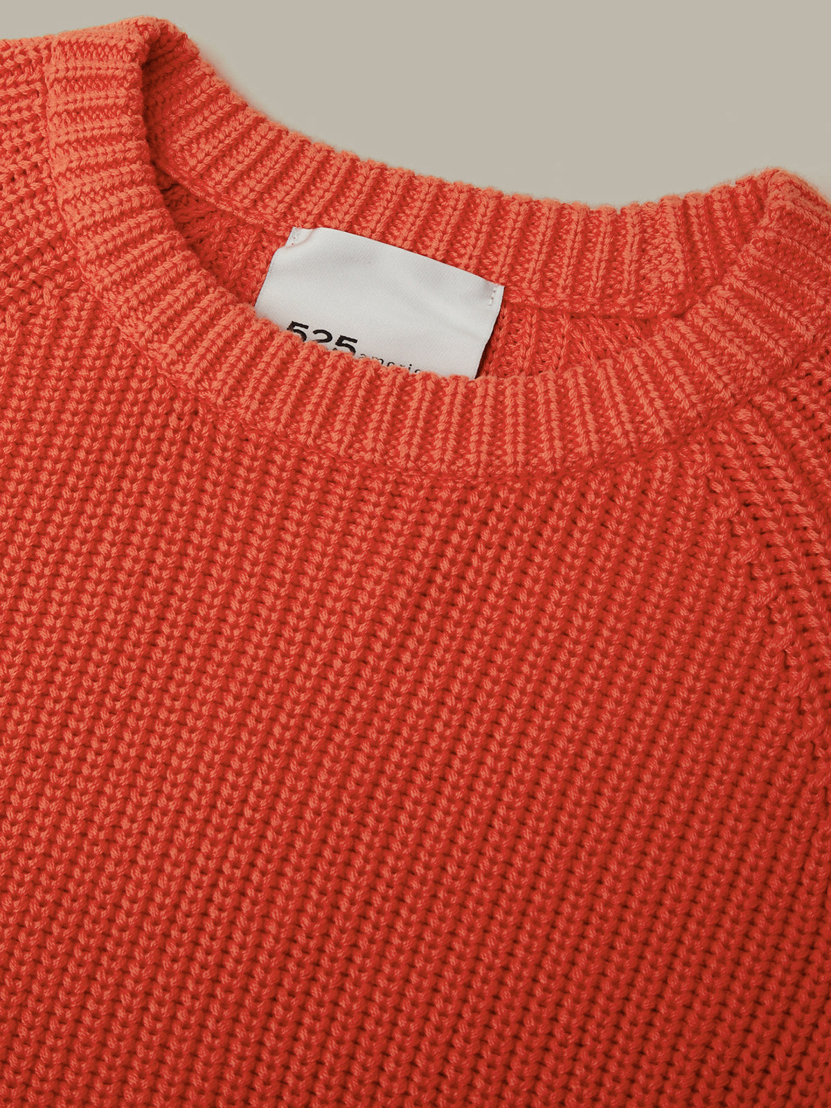 Close-up of a textured knit crewneck sweater in a warm rust-orange color, showing a white size tag inside the collar.
