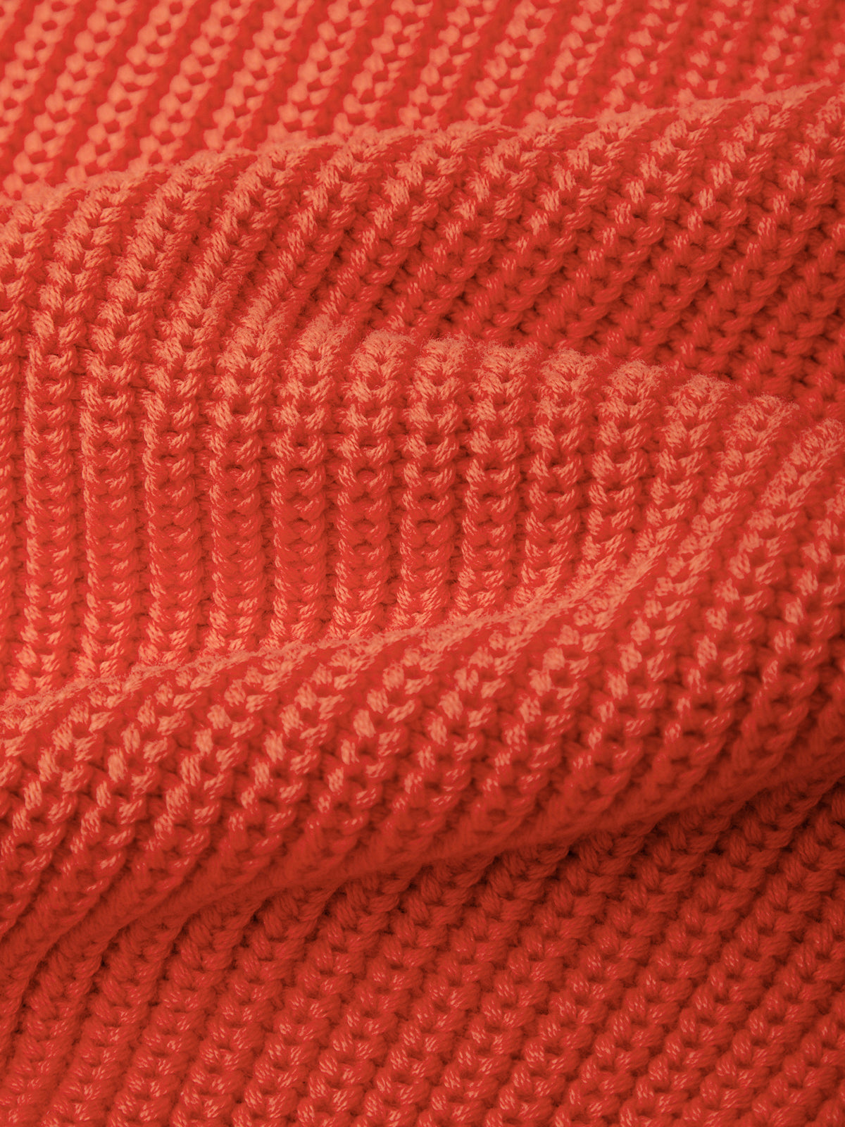 Close-up of a textured knit fabric in a warm coral-orange color, showing the ribbed stitch pattern and soft folds.