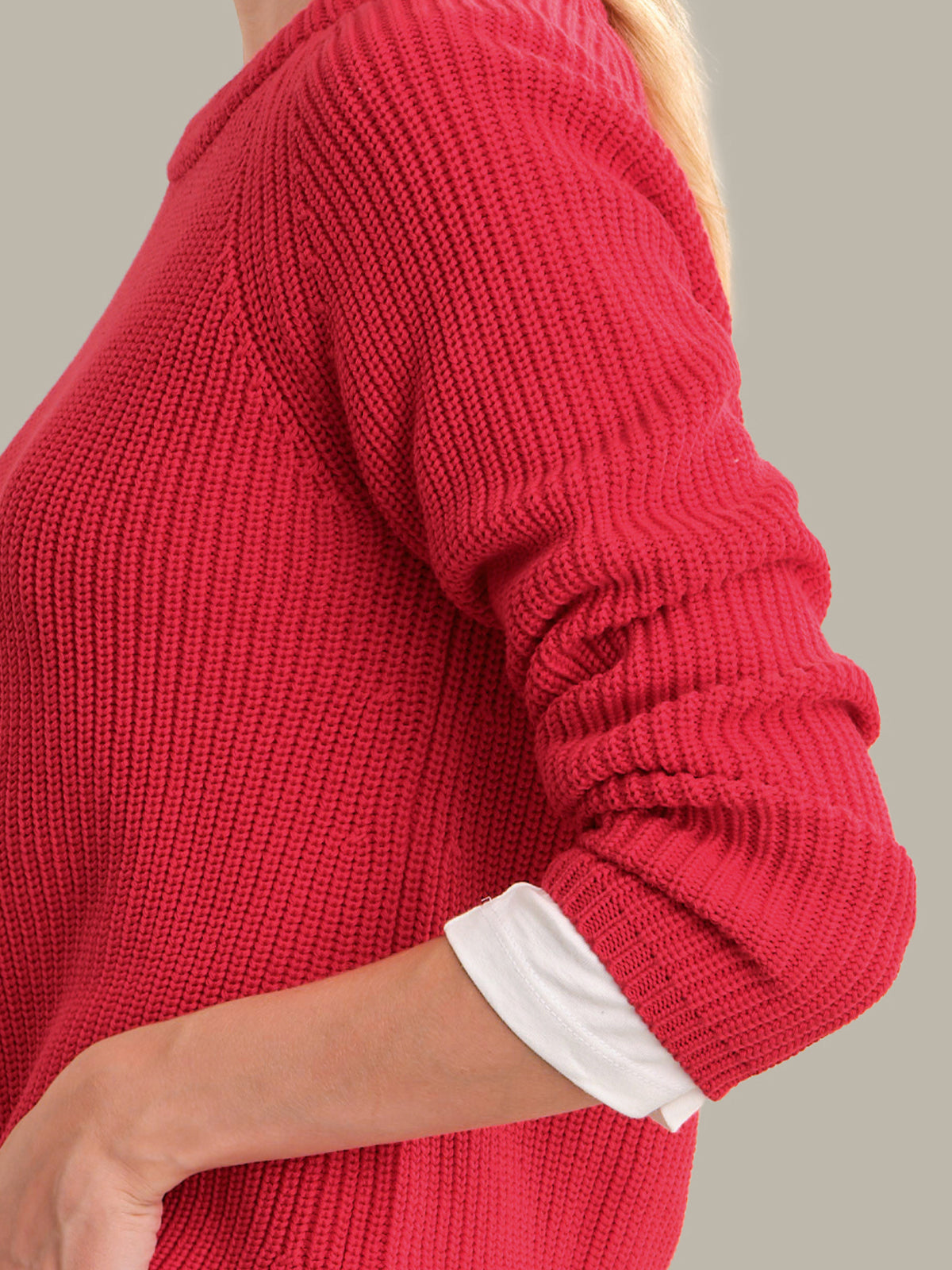 A close-up of a person wearing a bright red ribbed knit sweater over a white collared shirt, cropped from the neck down against a plain light gray background.