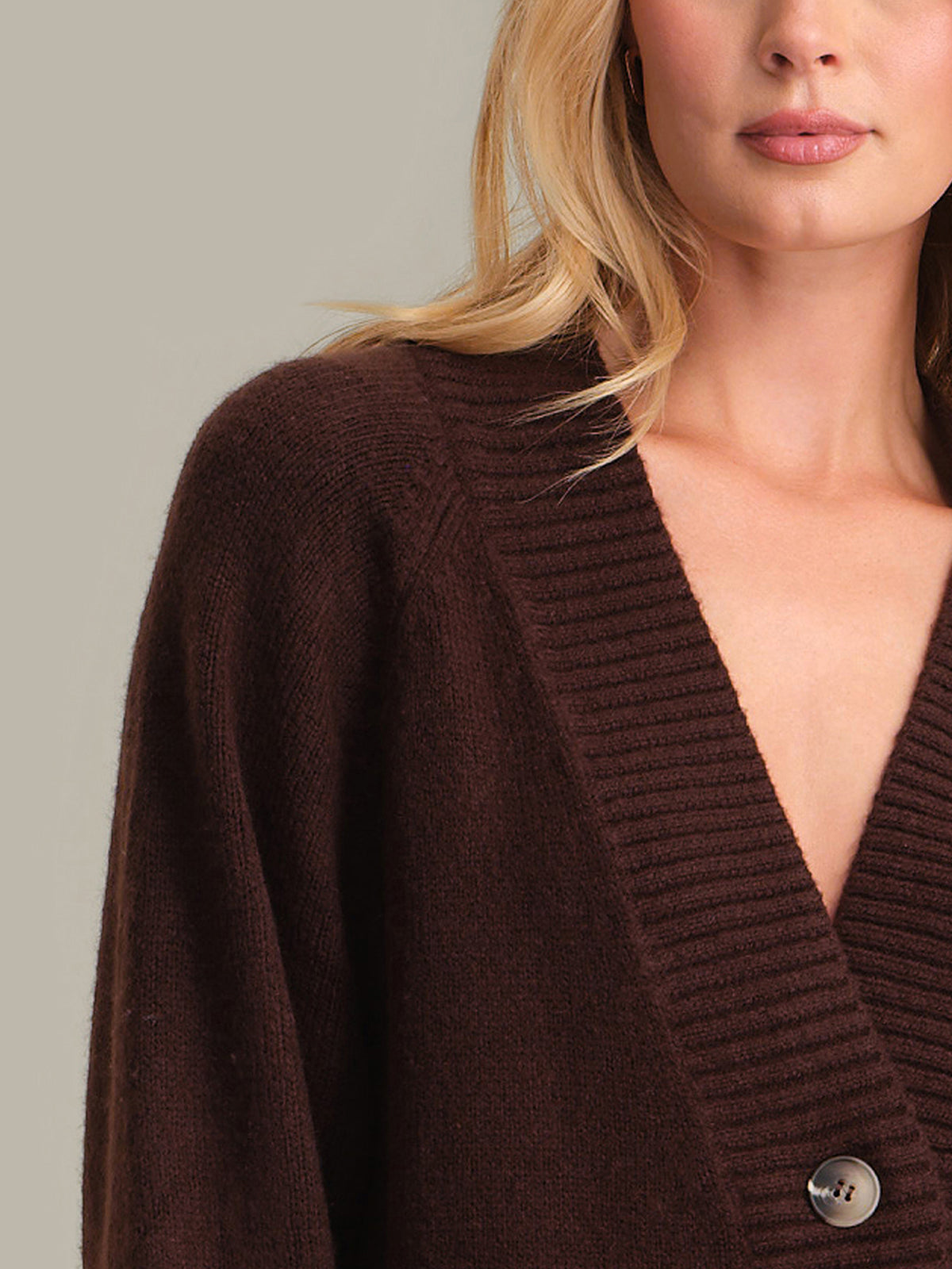 Brown sweater with a button detail worn by a person on a neutral background