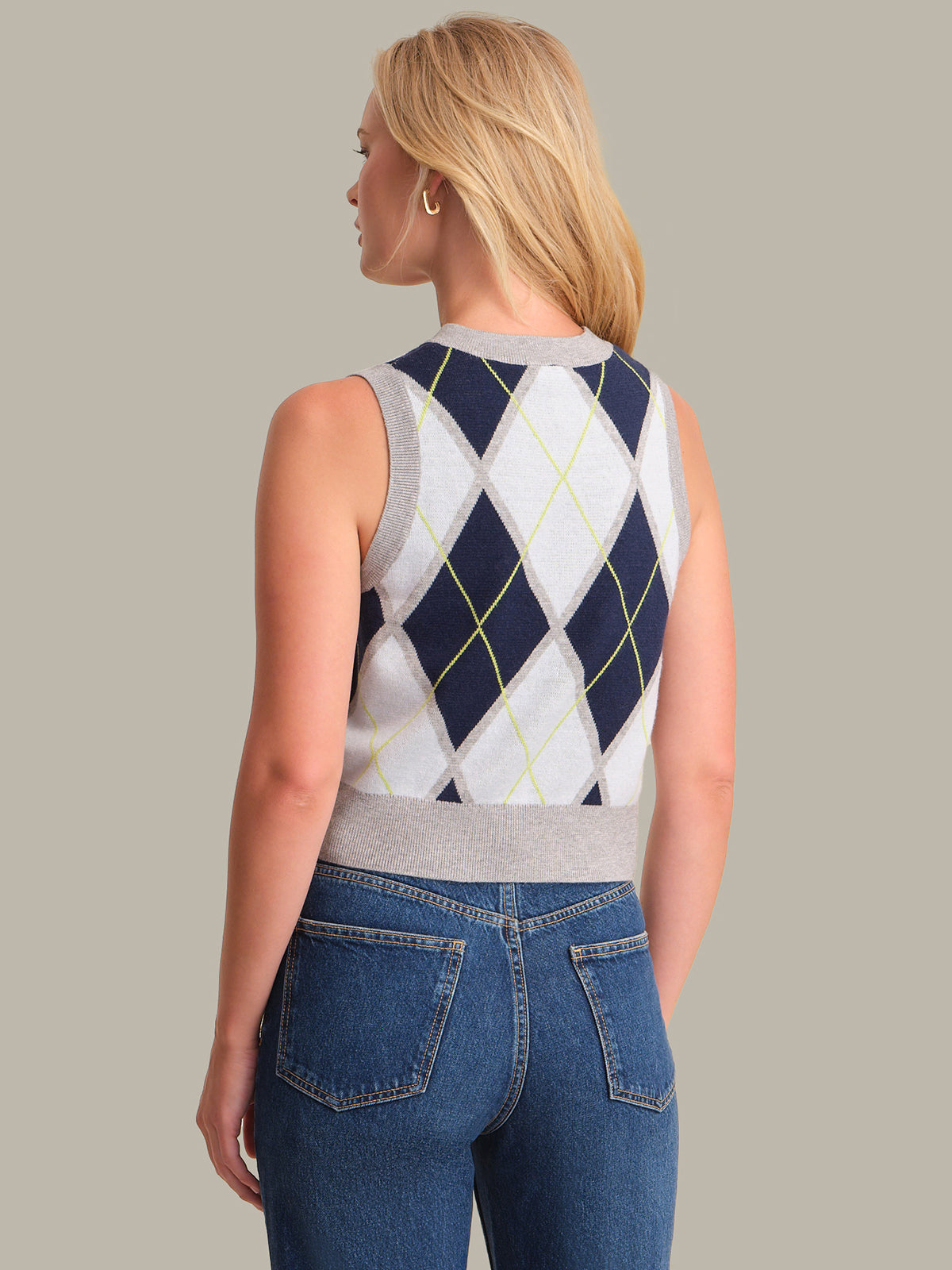 Woman wearing a sleeveless argyle sweater and blue jeans on a neutral background