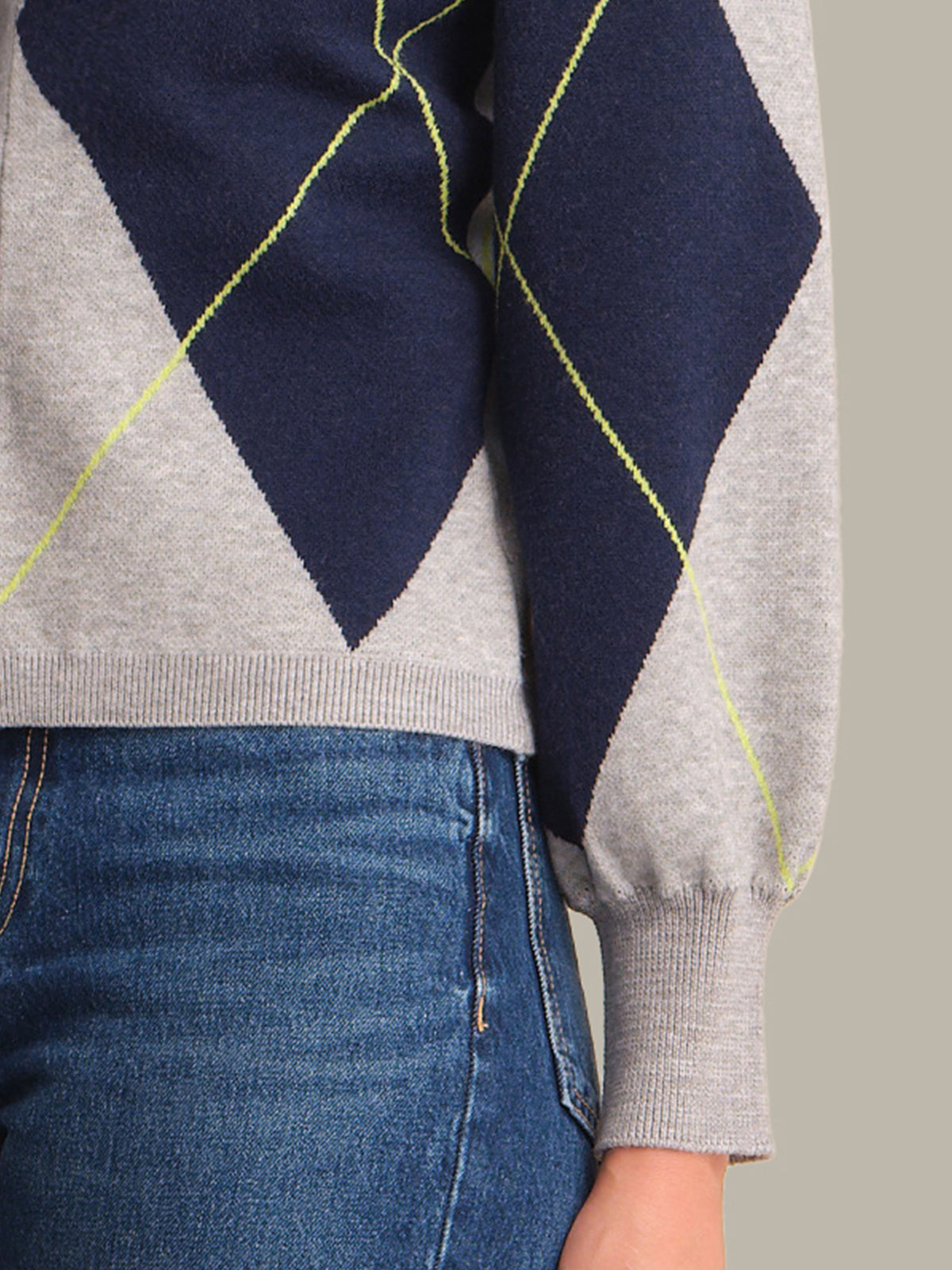 Gray sweater with navy and yellow diamond pattern worn over blue jeans on a neutral background