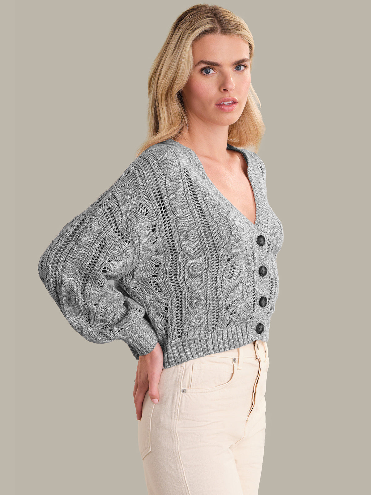 Woman wearing a gray knitted cardigan with black buttons on a plain background
