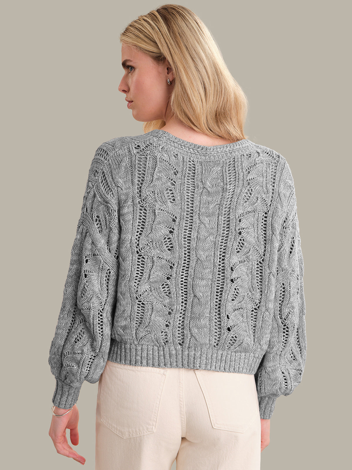 Woman wearing a gray cable knit sweater against a plain background