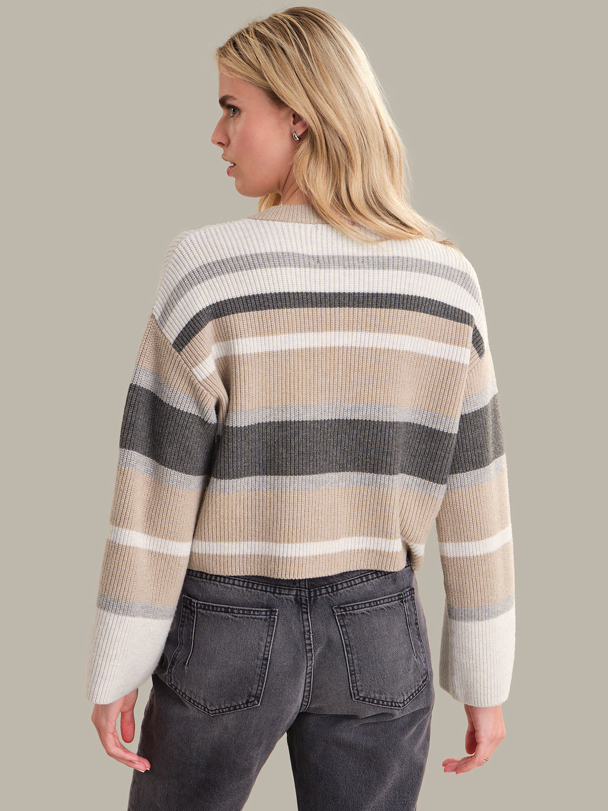 Woman wearing a striped sweater and gray jeans against a plain background