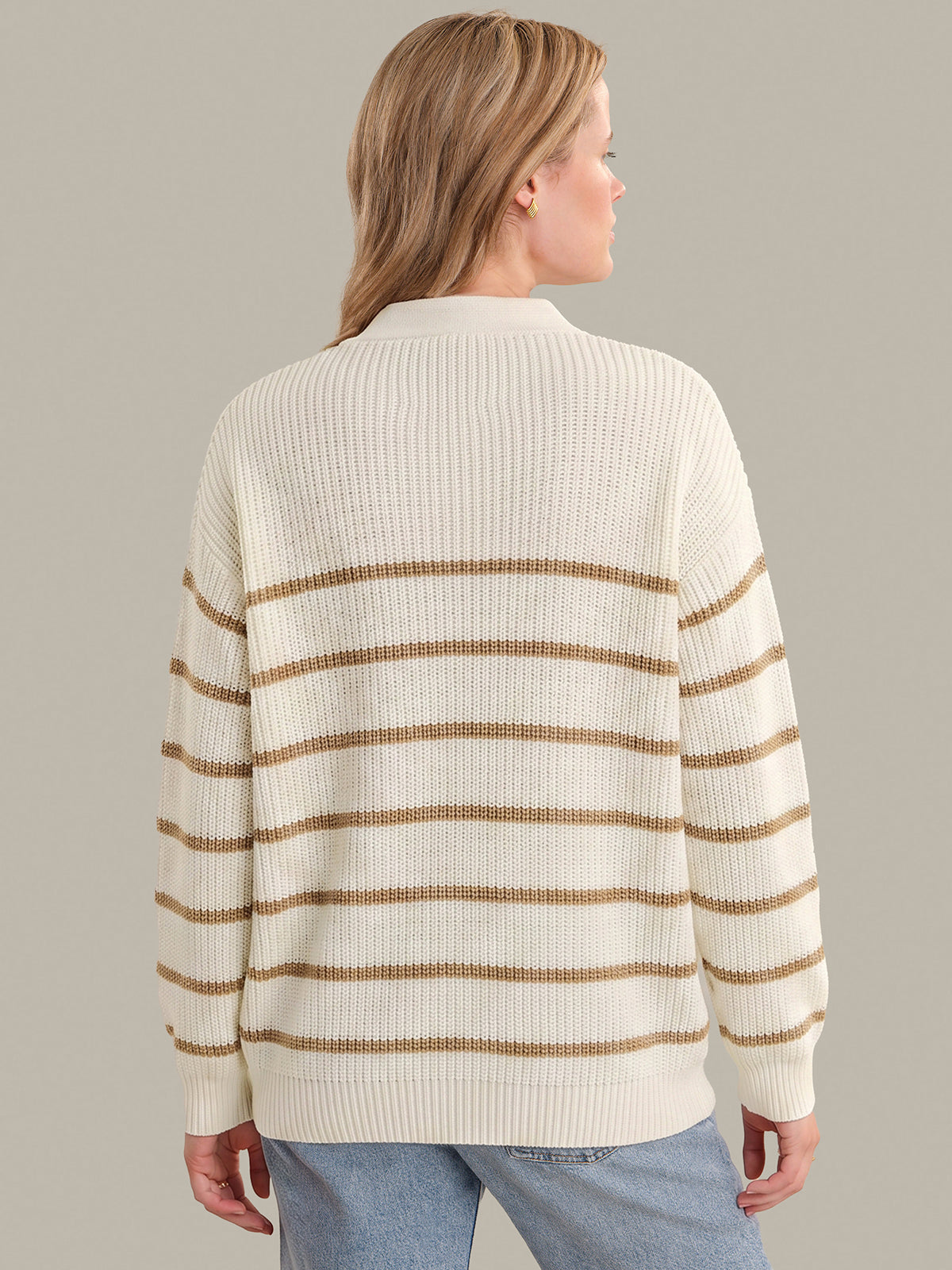 Woman wearing a cream and brown striped sweater on a gray background