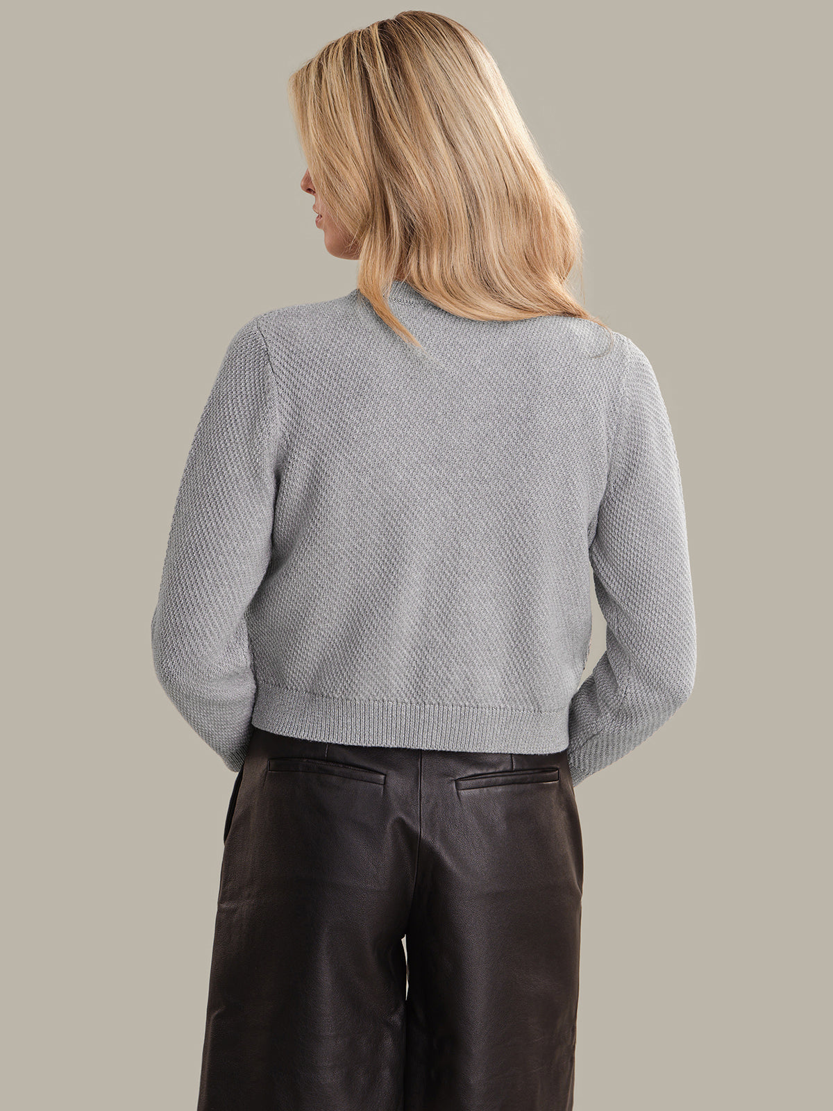 Person wearing a light gray textured sweater and dark pants on a beige background