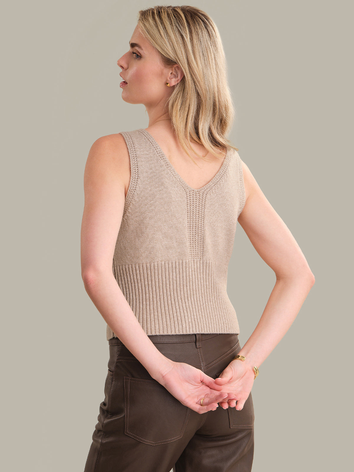 Woman wearing a beige sleeveless knitted top against a plain background