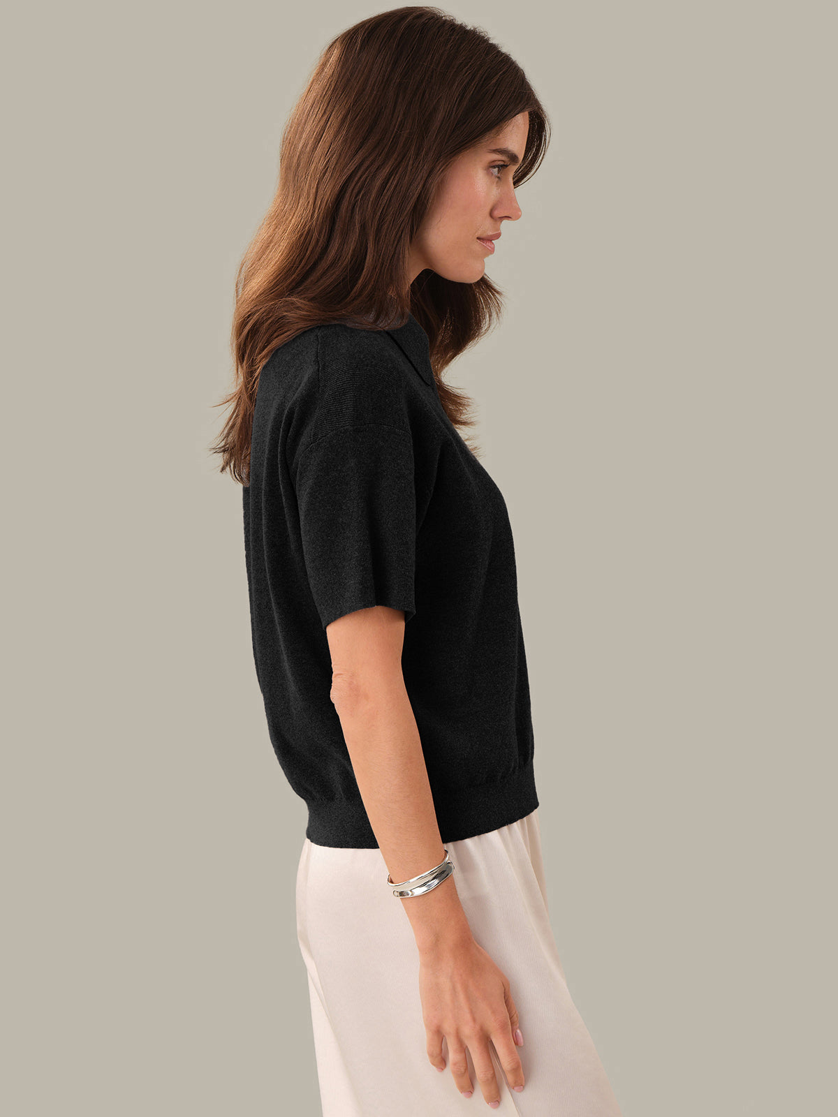 Woman wearing a black top and white pants against a plain background