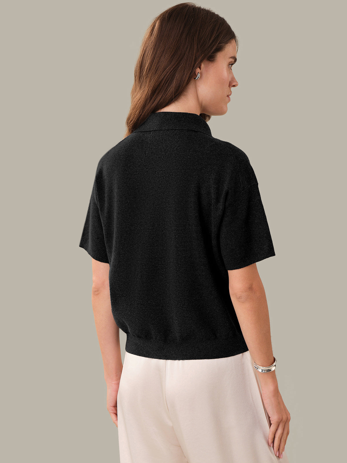 Woman wearing a black short-sleeve shirt and white pants on a gray background