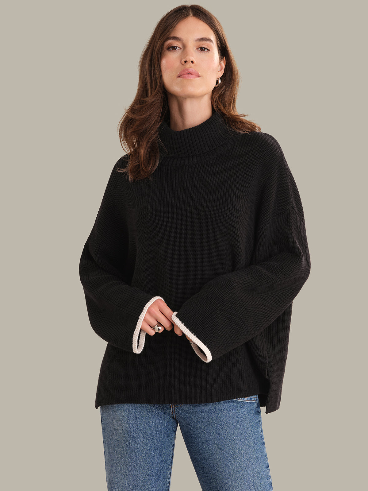 Woman wearing a black sweater and blue jeans against a plain background