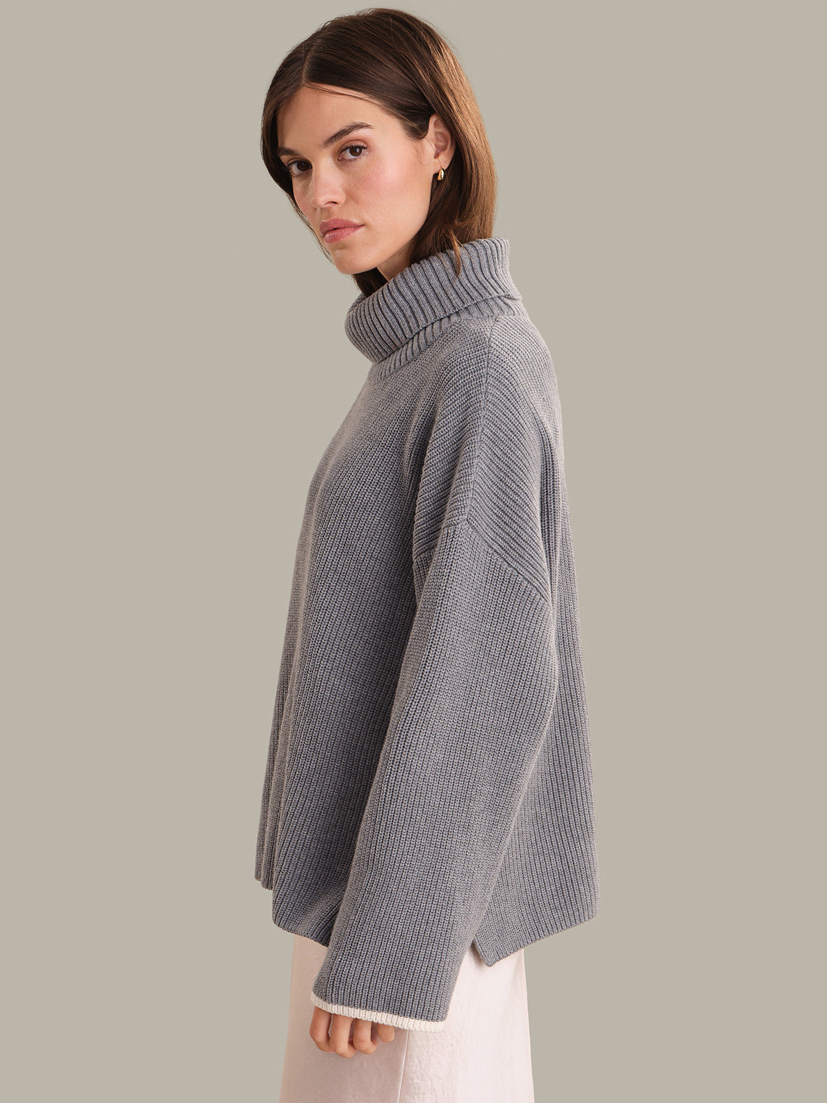 Woman wearing a gray turtleneck sweater against a plain background