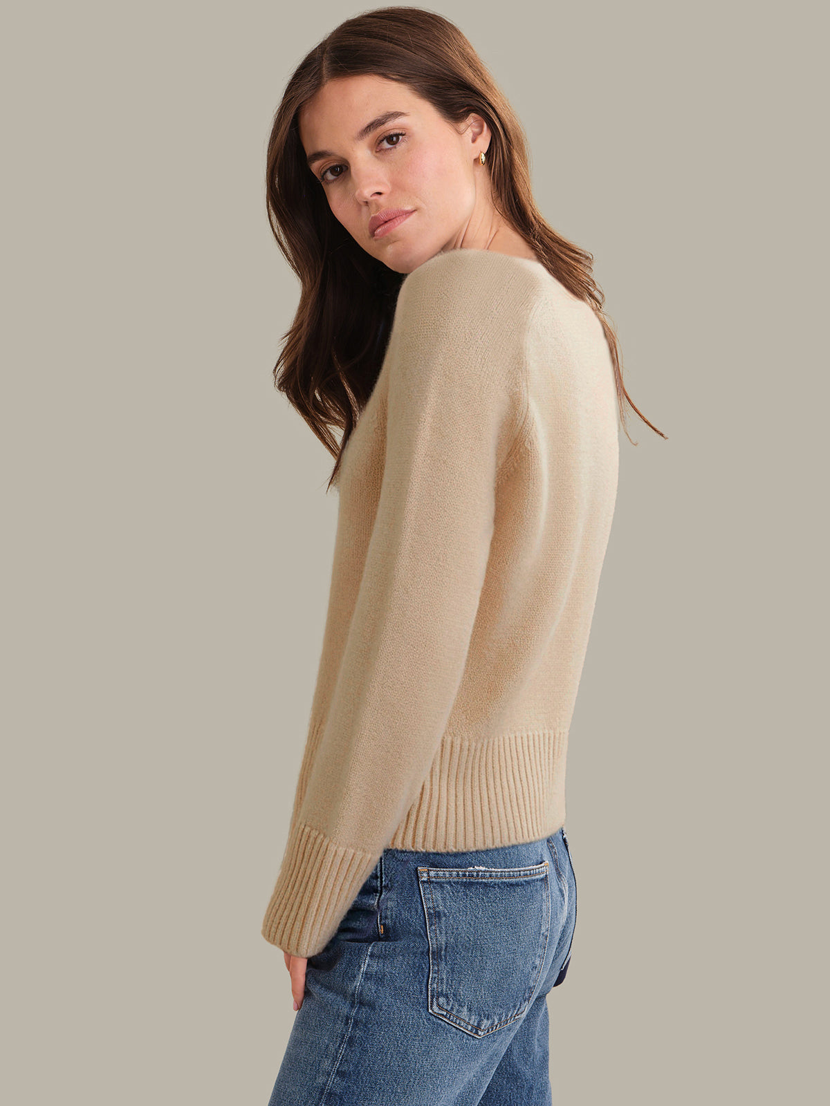 Woman wearing a beige sweater and blue jeans against a plain background