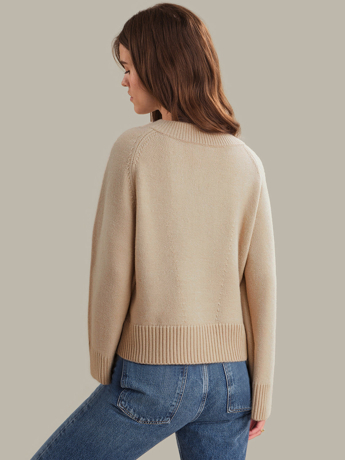 Woman wearing a beige sweater and blue jeans against a plain background