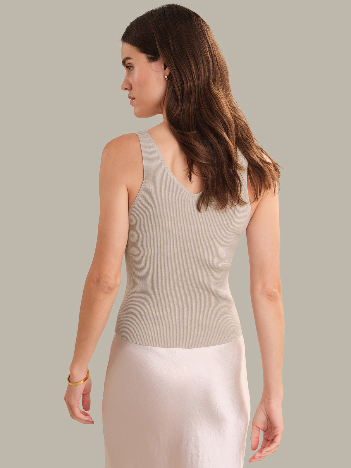 Woman wearing a beige sleeveless top against a neutral background