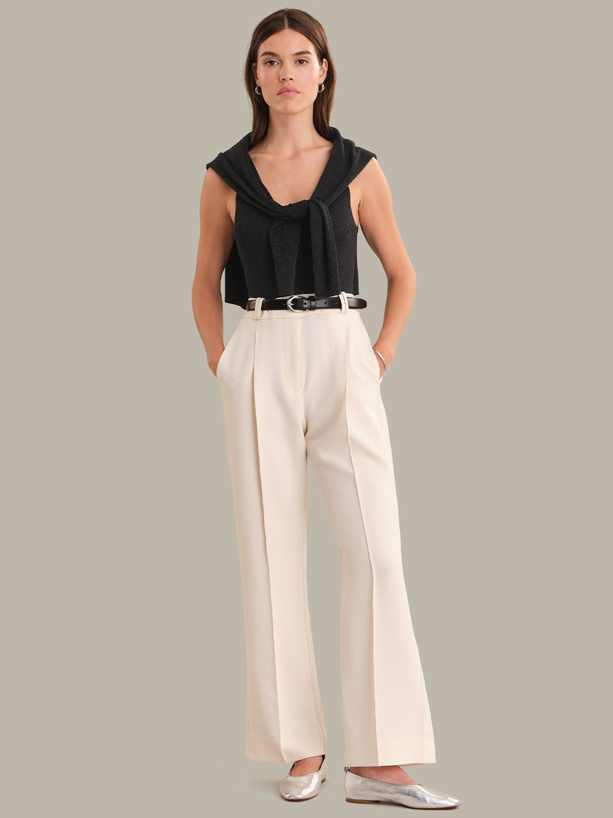 Woman wearing a black sleeveless top and white wide-leg pants on a gray background