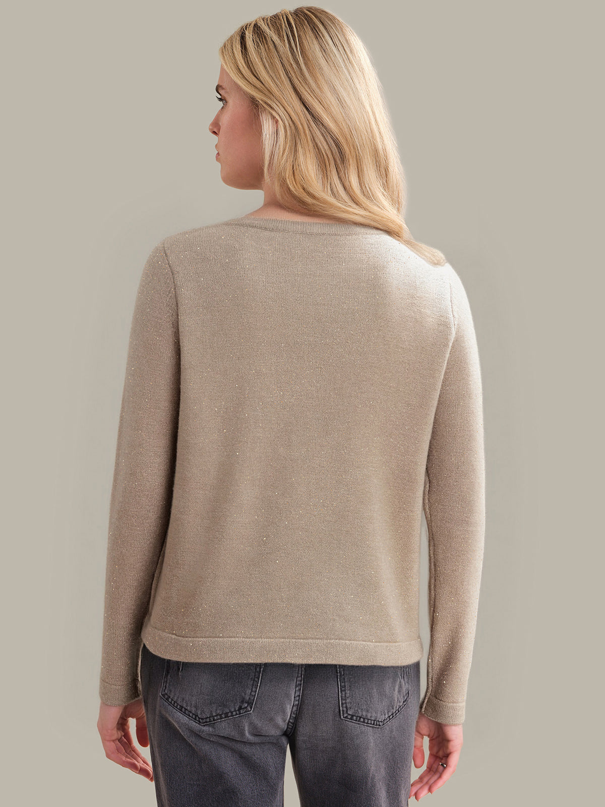 Woman wearing a beige sweater and dark jeans against a plain background